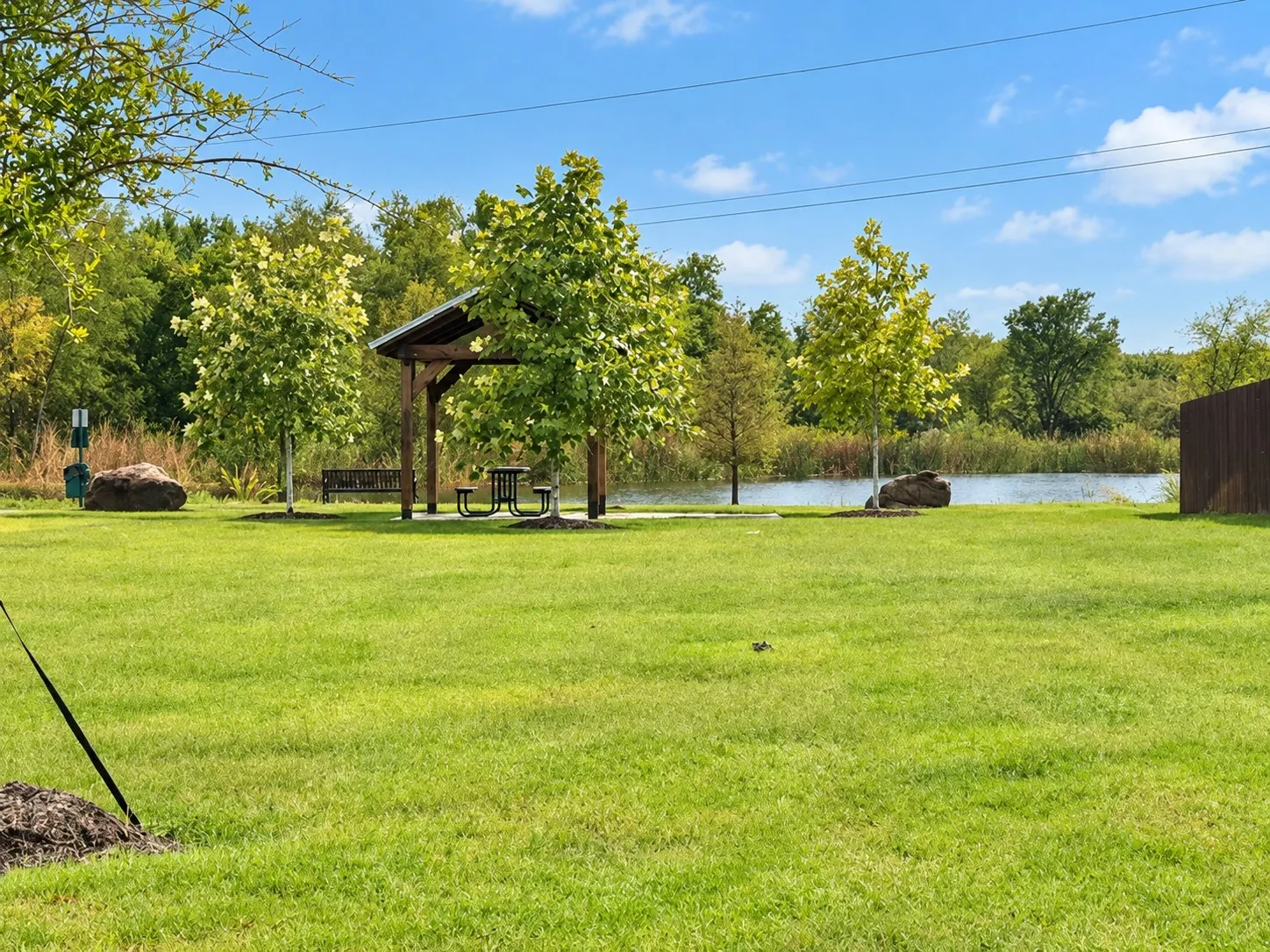 Expansive green lawn with mature trees, a covered picnic area, and a tranquil pond