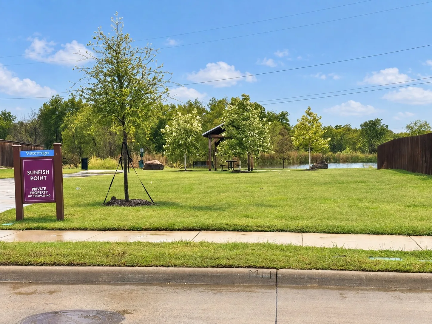 Expansive green space featuring a water element, mature trees, and a wooden gazebo