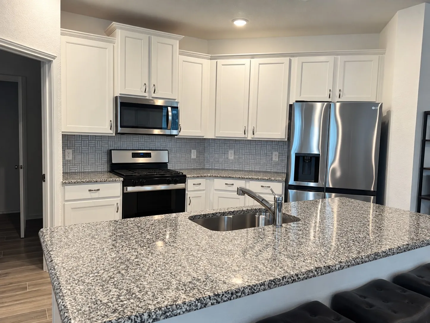 Kitchen featuring white shaker cabinetry, stainless steel appliances, patterned tile backsplash, and granite countertops