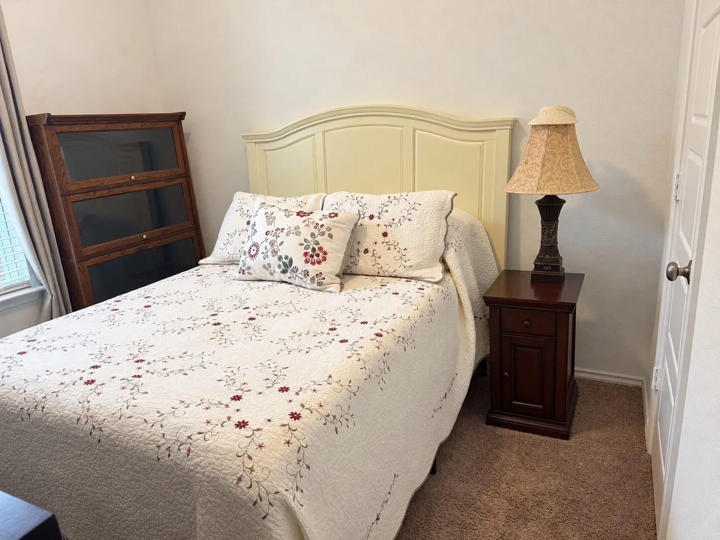 Carpeted room featuring a window with blinds, a solid door, and a light-colored headboard