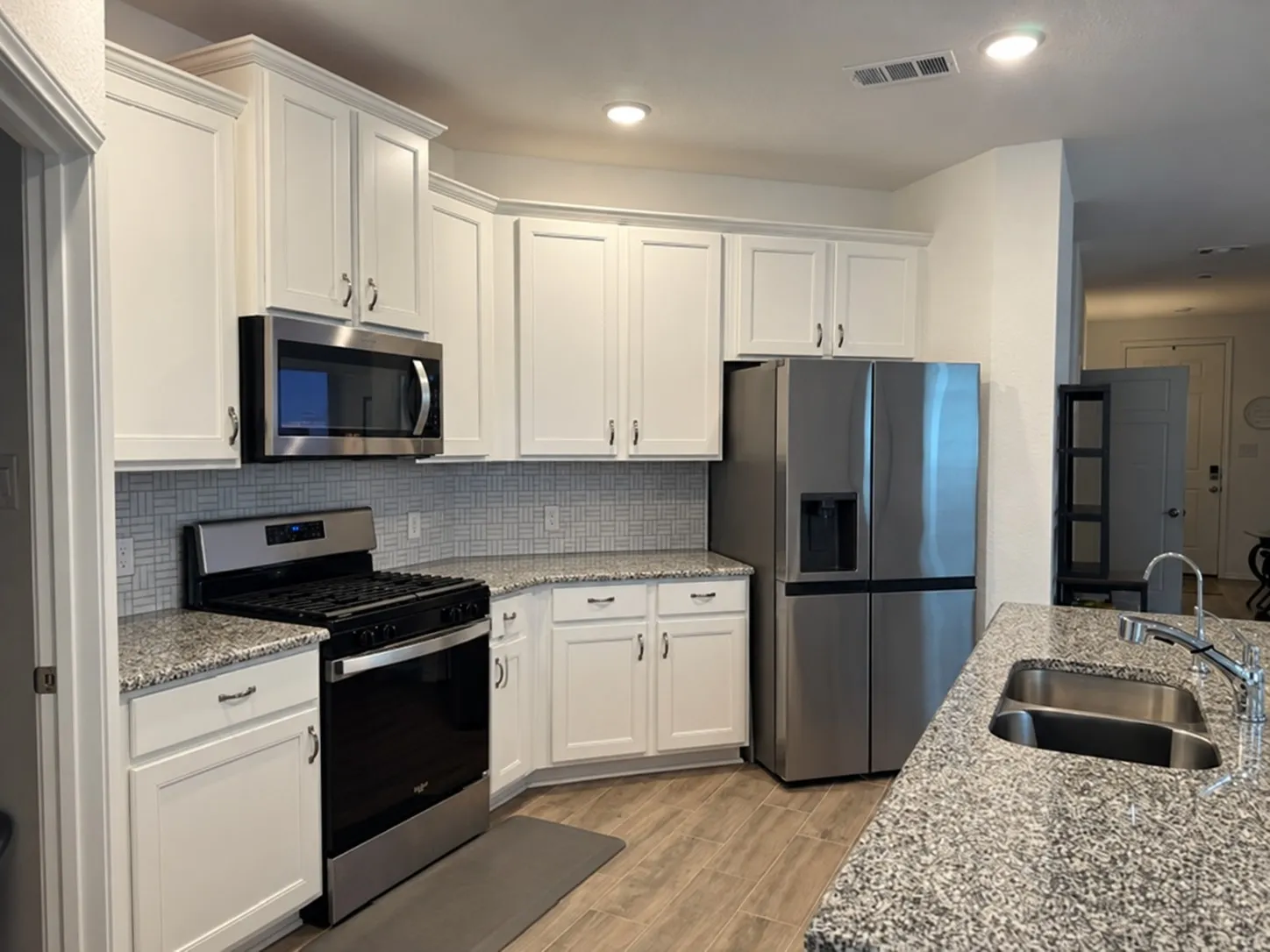 White cabinetry with crown molding, stainless steel appliances, granite-style countertops, mosaic tile backsplash, and wood-finish flooring