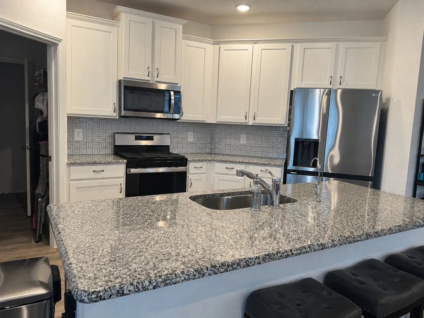Kitchen featuring white cabinetry, stainless steel appliances, speckled stone countertops, and a tiled backsplash