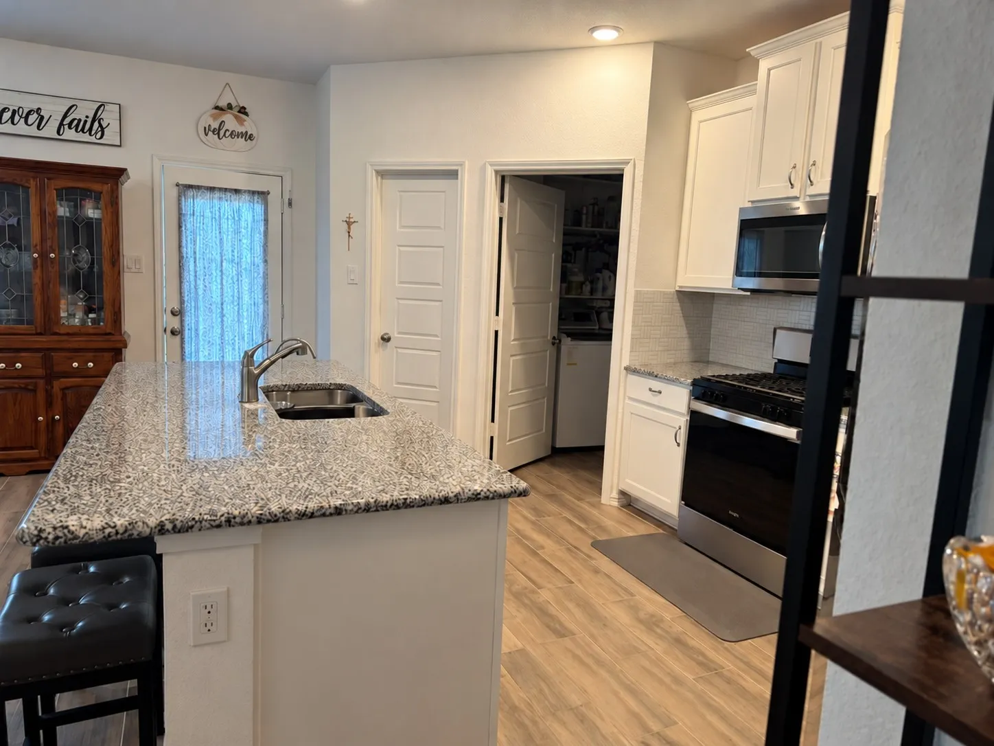 Kitchen featuring a central island with an integrated sink, light-toned countertops, white cabinetry, wood-finish flooring, and a subway tile backsplash