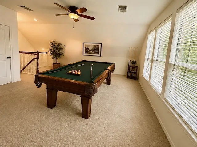 Carpeted loft space with sloped ceilings, multiple windows with blinds, a ceiling fan, and a white interior door