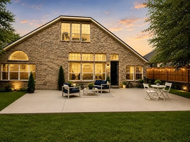 Expansive brick exterior with a large concrete patio, manicured lawn, and multi-pane windows
