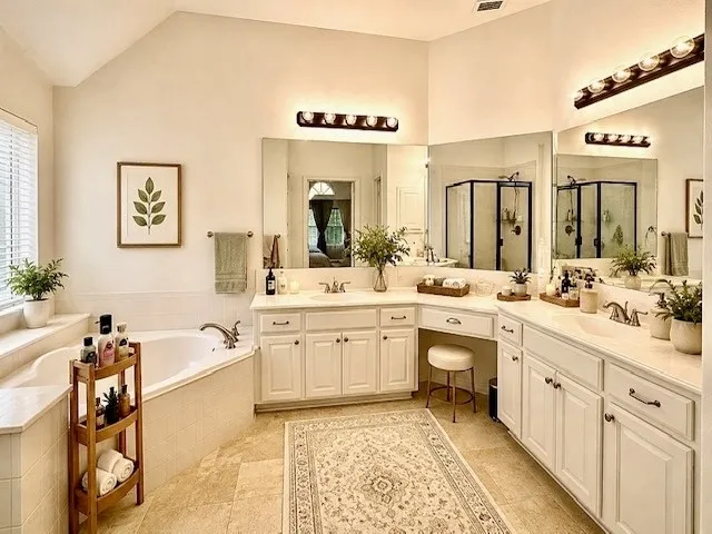 Vaulted ceiling, corner soaking tub, dual vanities with integrated sinks, built-in vanity area, and a glass-enclosed shower