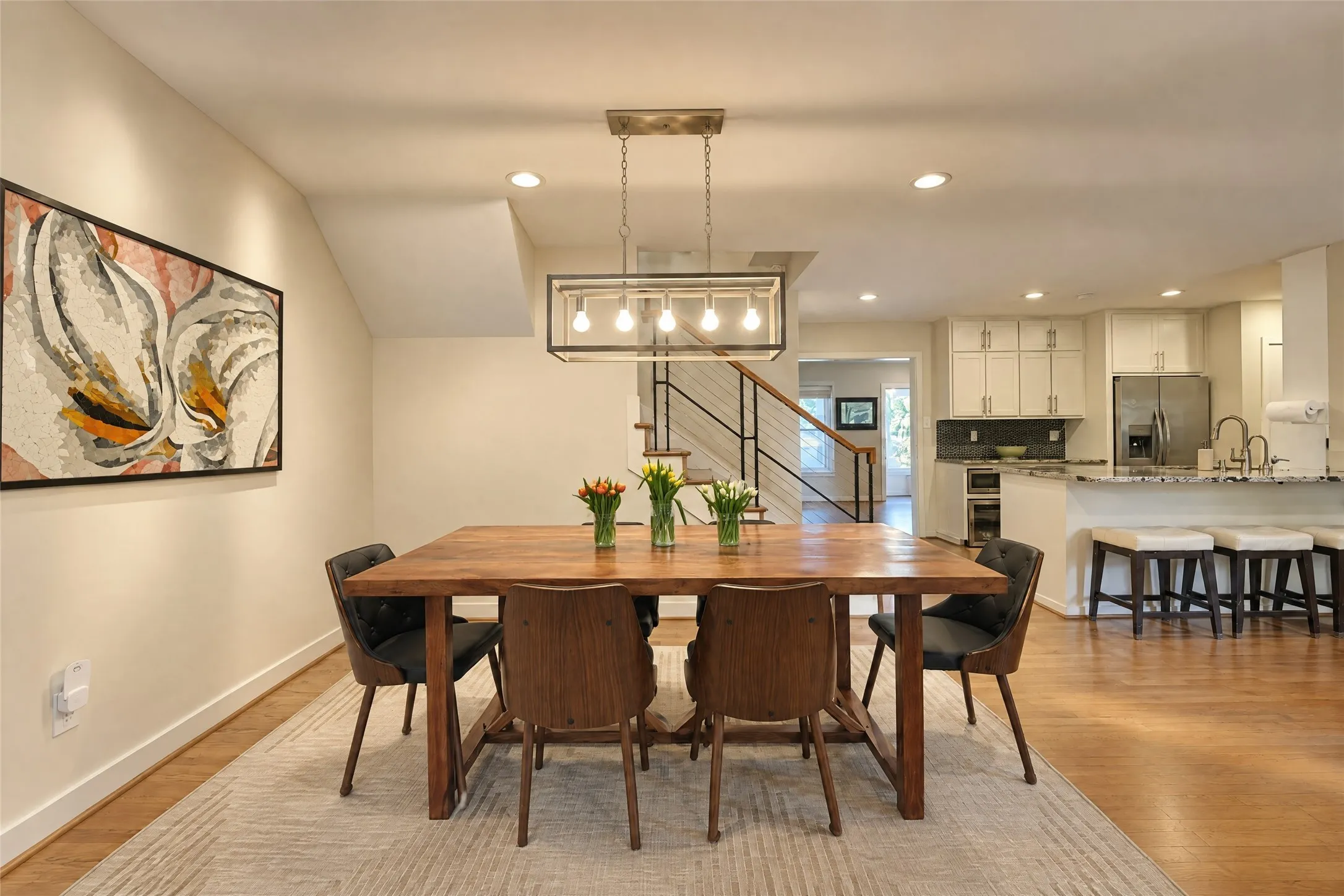 Open-concept dining area with wood-finish flooring, recessed lighting, and a linear chandelier