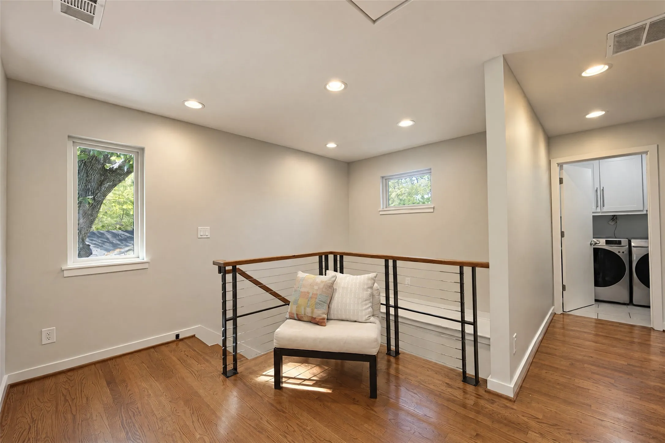 Hardwood flooring, recessed ceiling lighting, cable railing system, built-in laundry area with cabinetry, and multiple windows