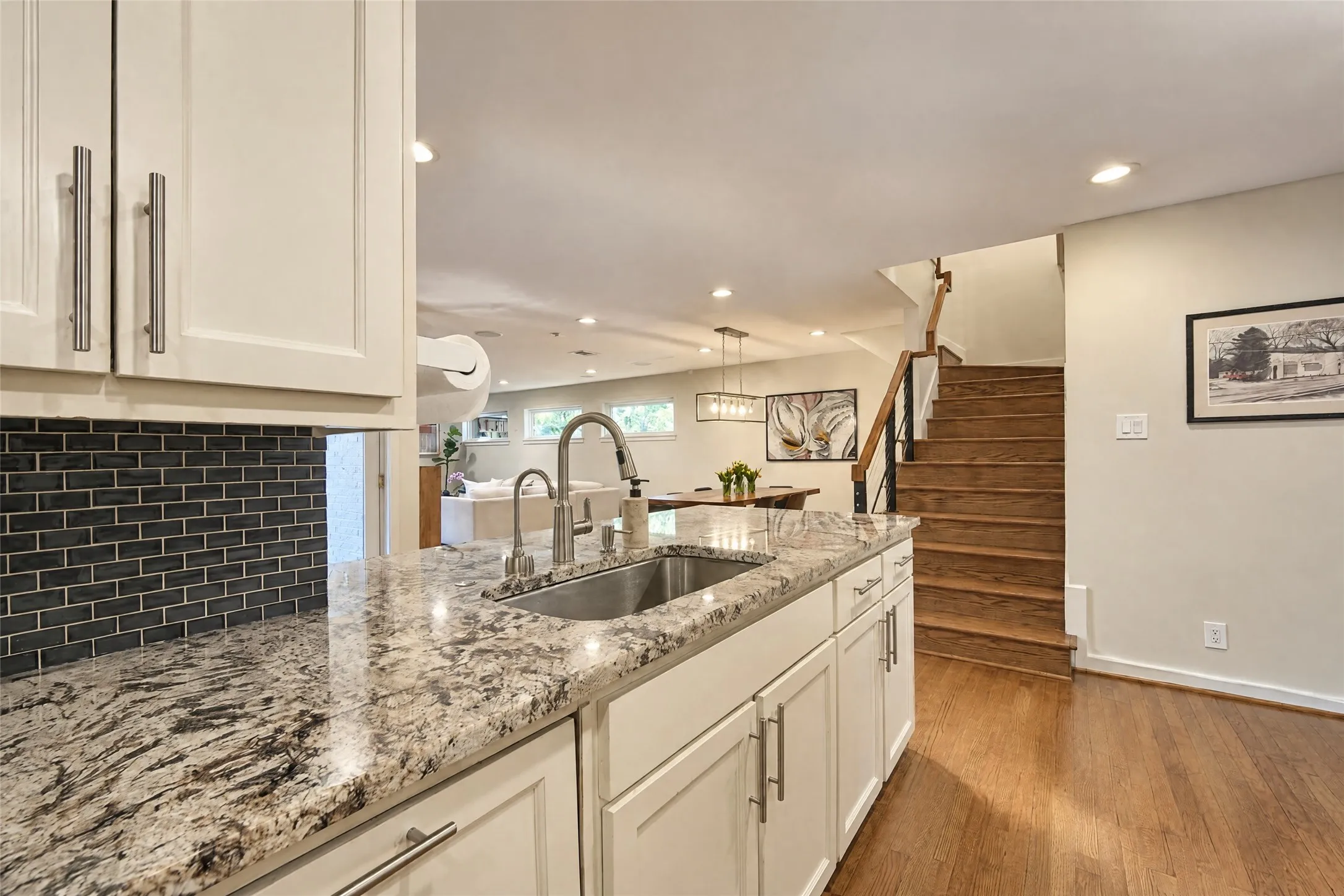 Kitchen island featuring a stainless steel sink, pull-down faucet, and light-toned stone countertops with dark veining