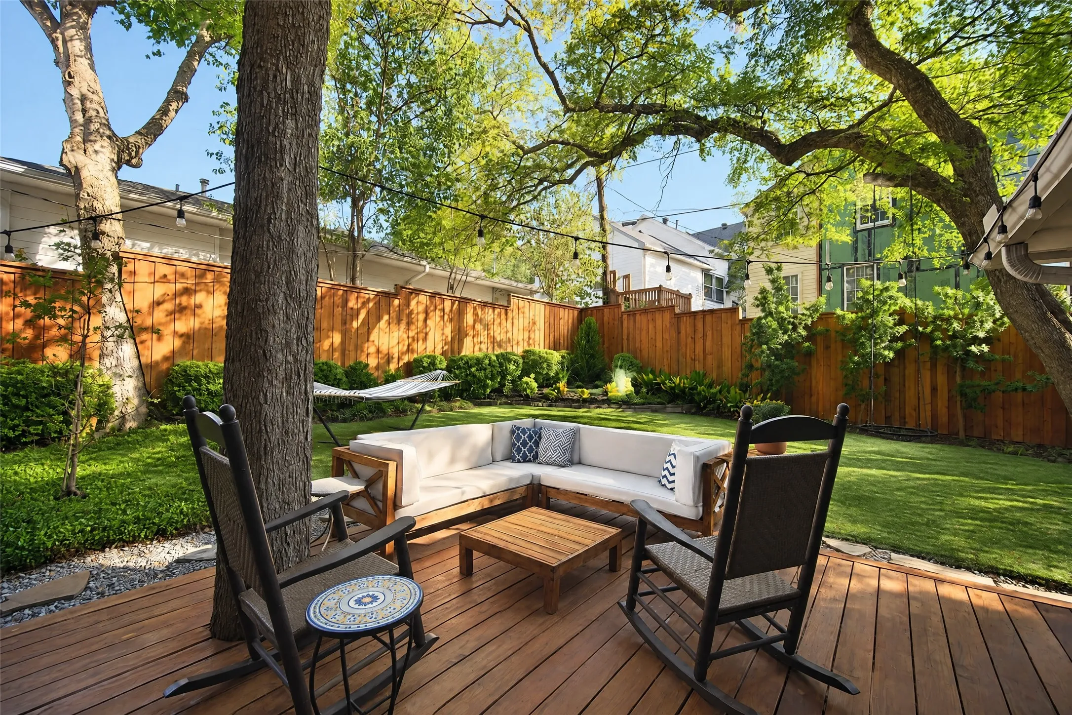 Expansive backyard with a wood deck, string lighting, mature trees, manicured lawn, and wood privacy fencing