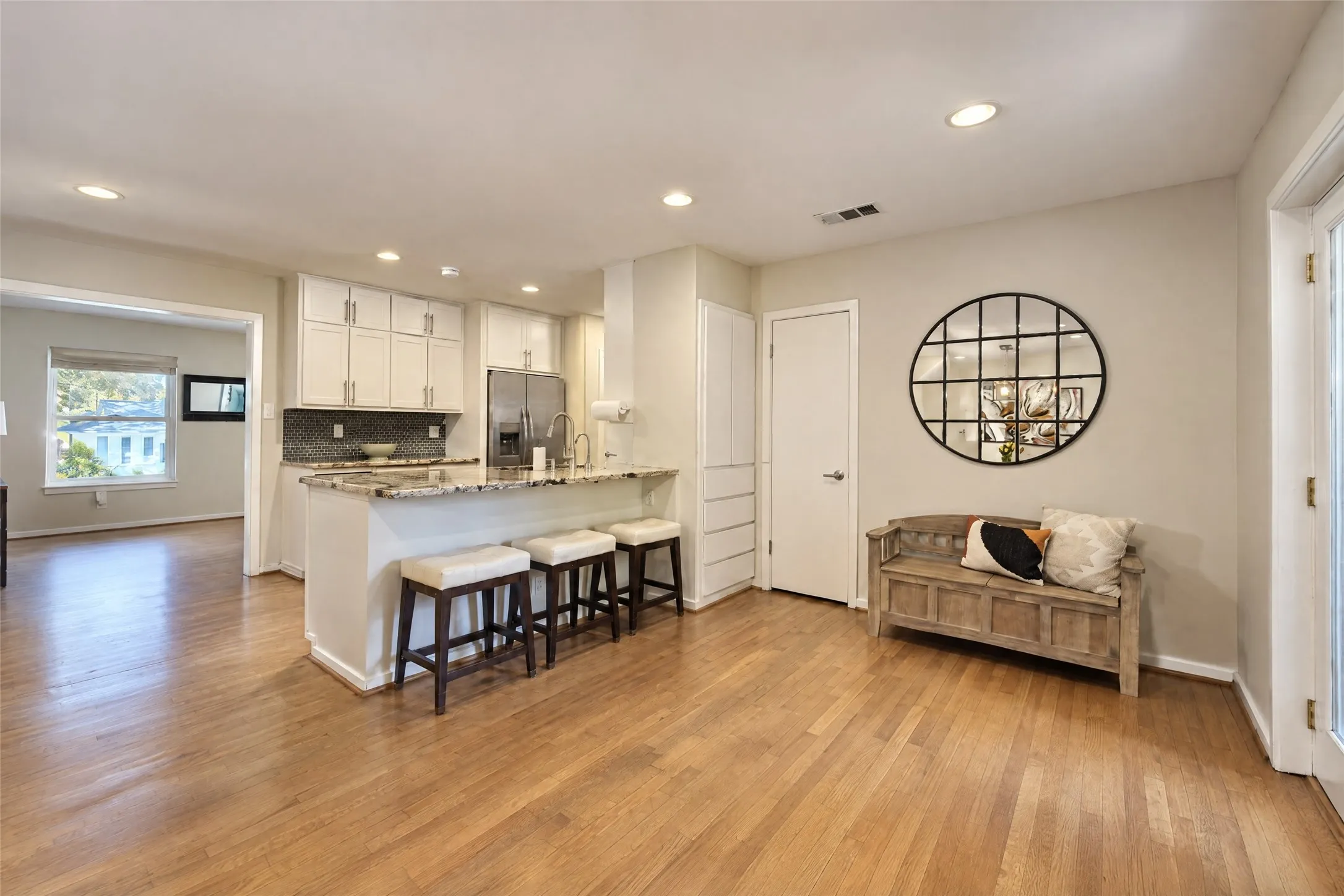 Hardwood-finish flooring throughout, recessed ceiling lighting, kitchen island with stone countertop, stainless steel appliances, and white cabinetry