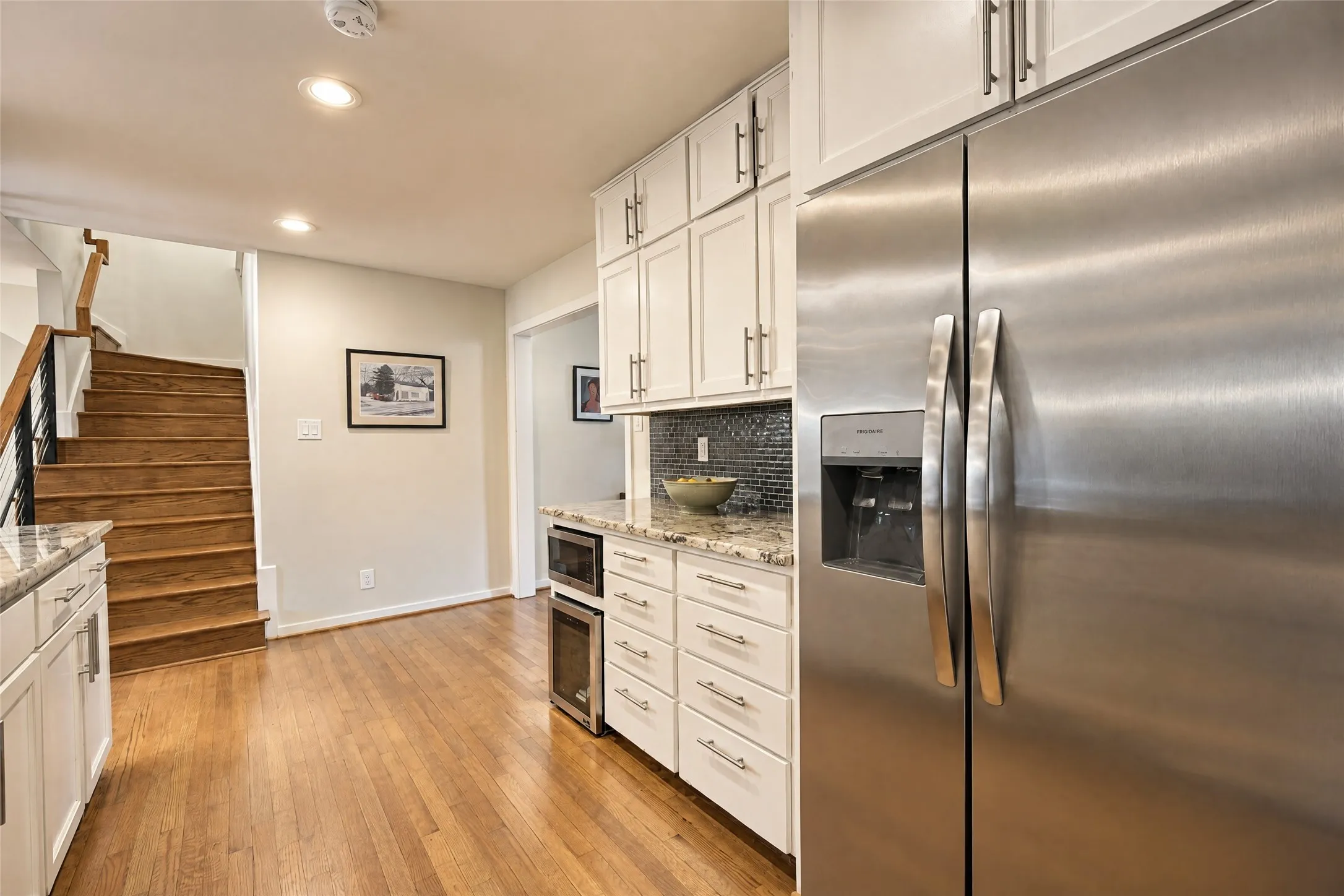 Stainless steel refrigerator, white cabinetry, granite countertops, tile backsplash, and wood flooring