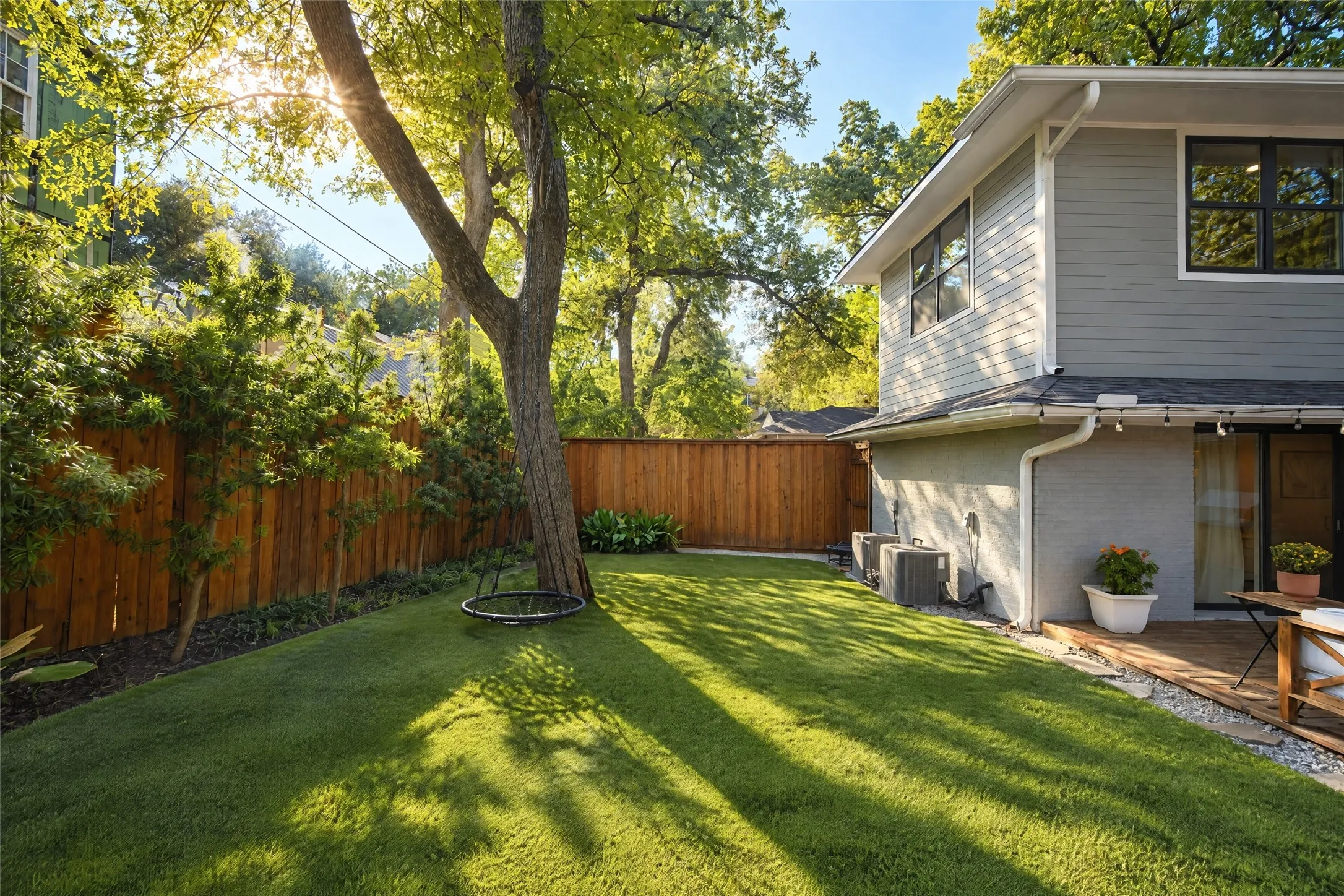 Expansive lawn area with mature trees, bordered by a wooden privacy fence and established plantings