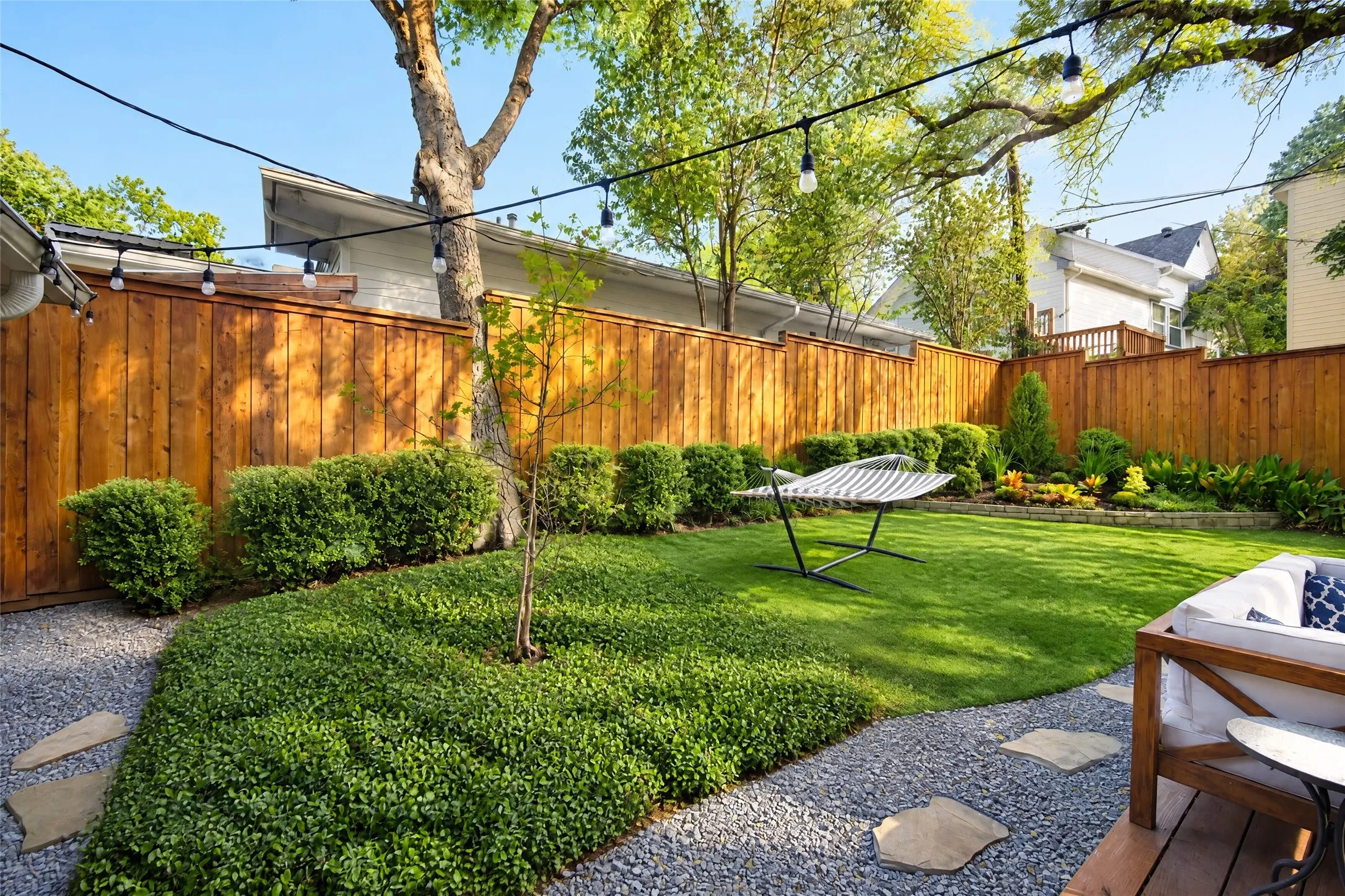 Fenced backyard featuring natural wood fencing, a manicured lawn, established landscaping, and a gravel path with stepping stones