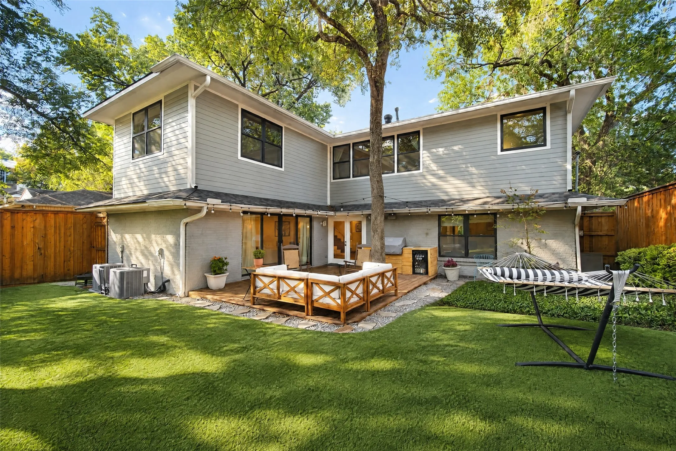 Expansive green lawn with a wood-plank deck, mature trees, and a privacy fence