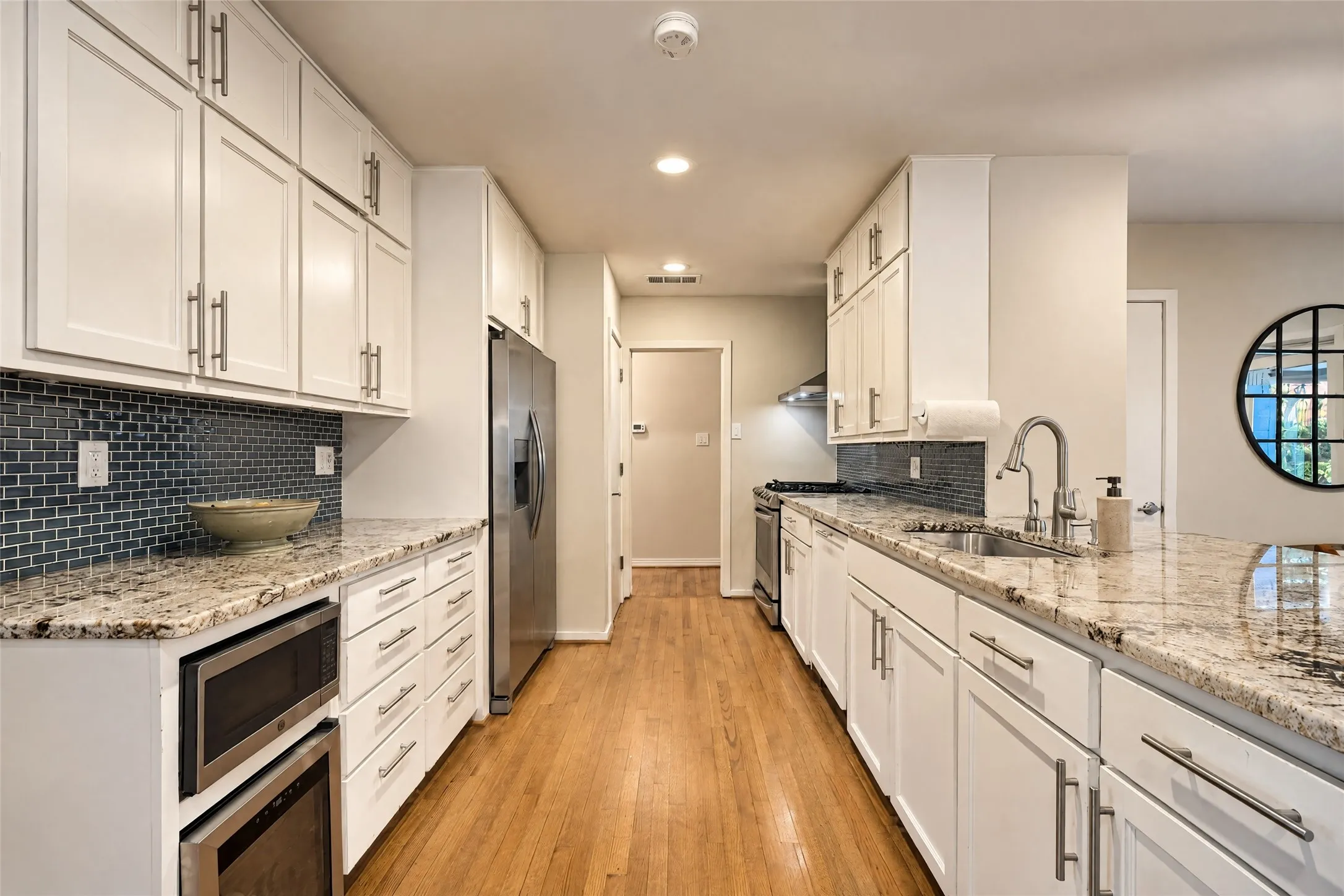 White shaker cabinetry, granite countertops, subway tile backsplash, stainless steel appliances, and wood-finish flooring