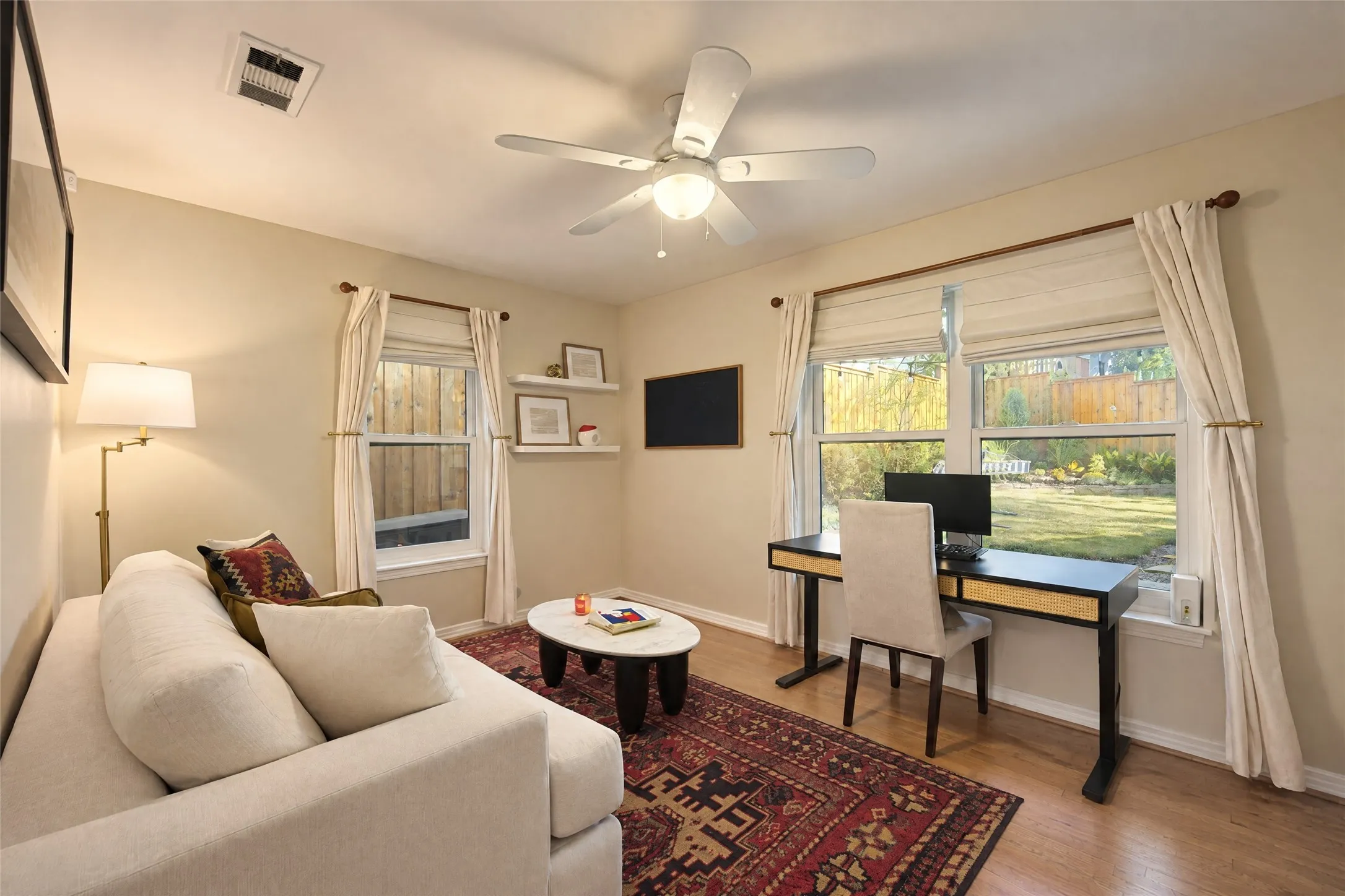 Wood-finish flooring, multiple windows with neutral window treatments, and a ceiling fan with integrated lighting