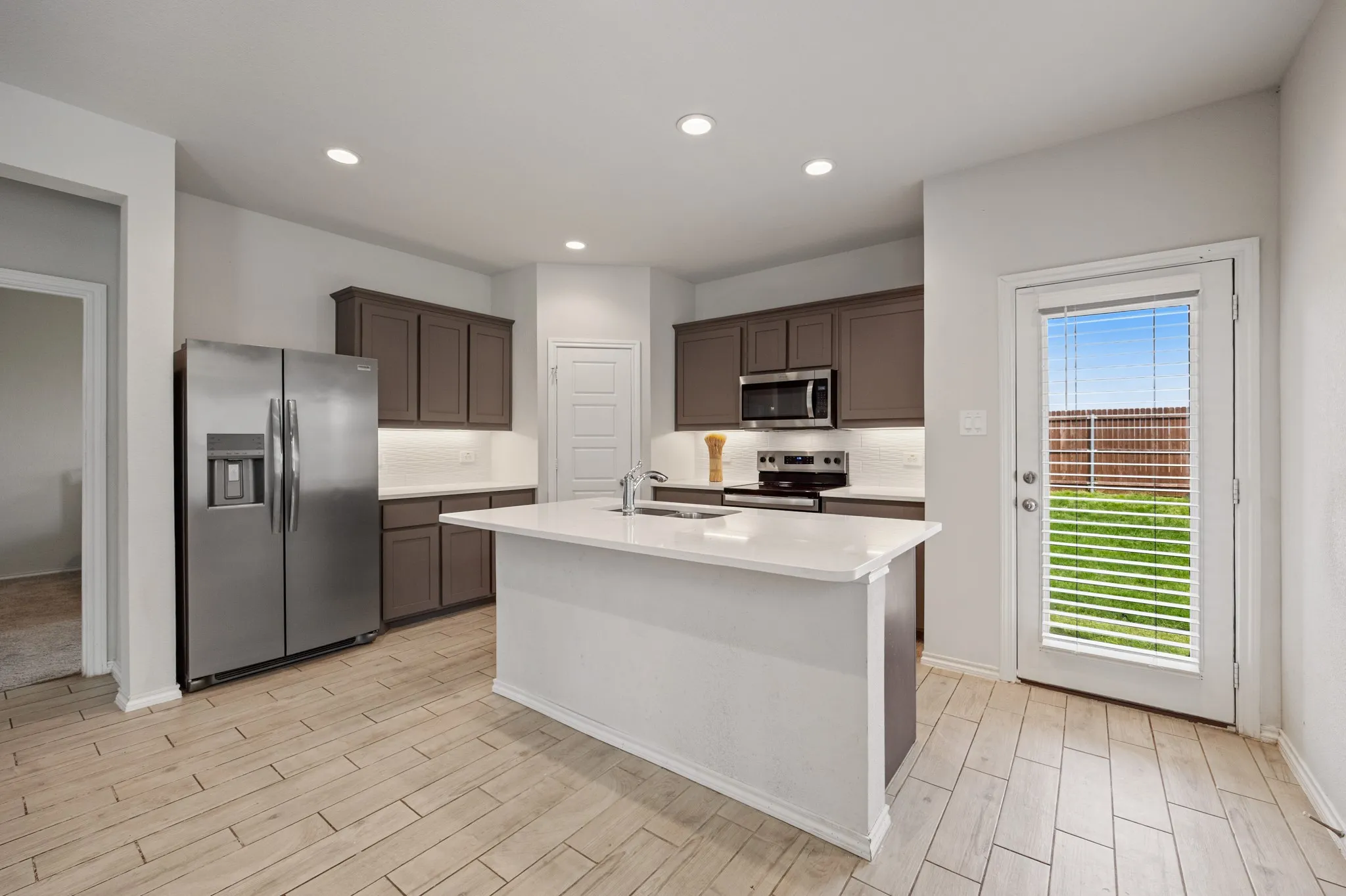 Kitchen featuring an island with a built-in sink, wood-finish tile flooring, recessed lighting, and dark wood cabinetry