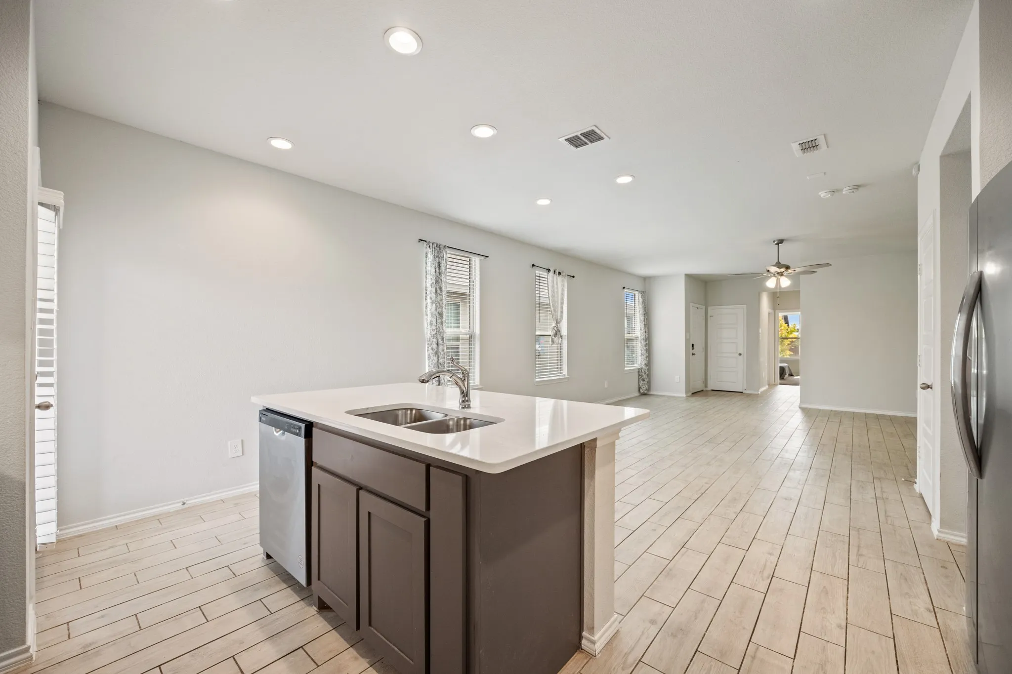Open-concept living area featuring an island with a double basin sink, stainless steel dishwasher, and light-toned tile flooring
