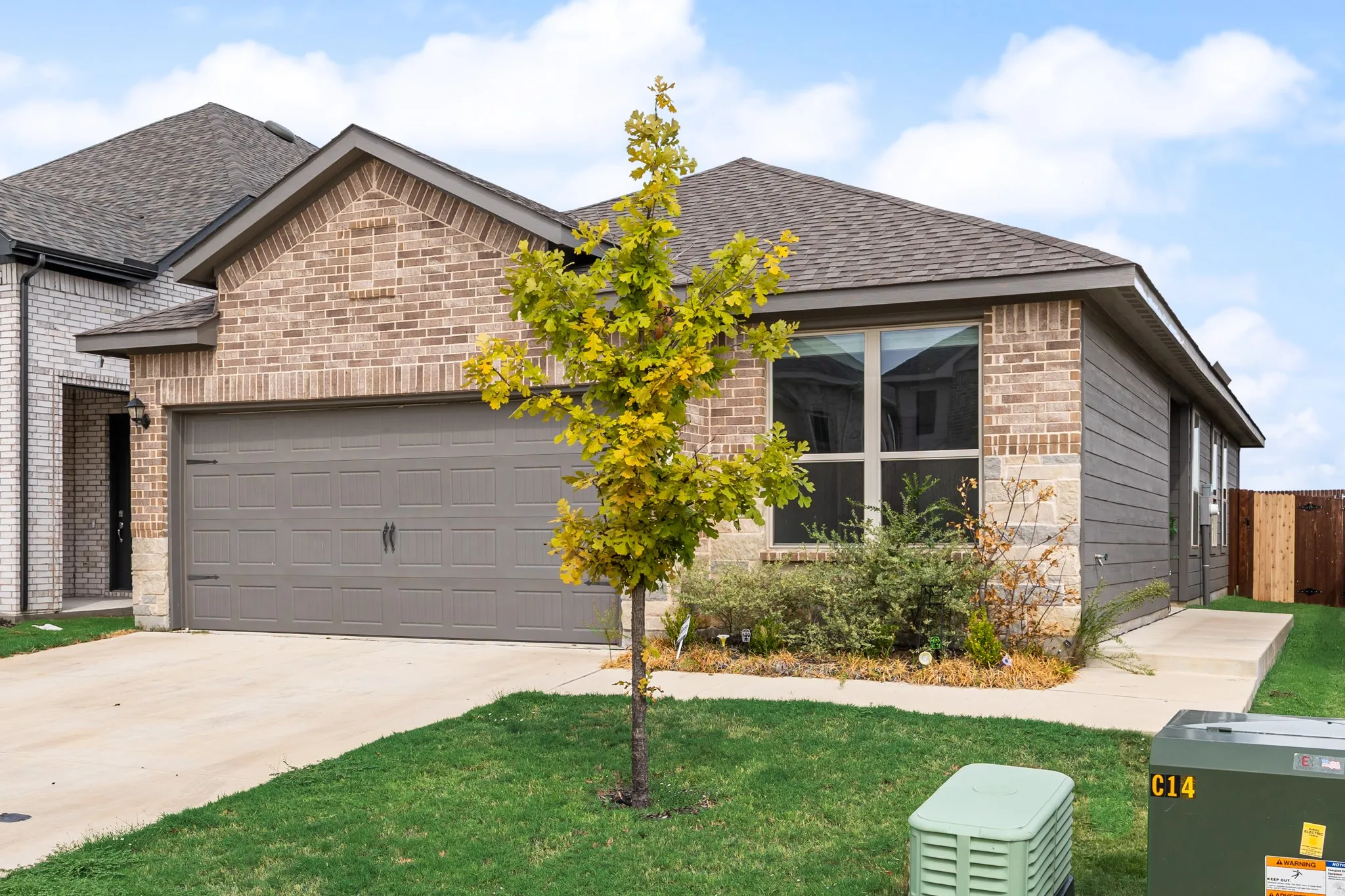 Brick and stone façade with horizontal siding accents, attached two-car garage, concrete driveway, and mature landscaping