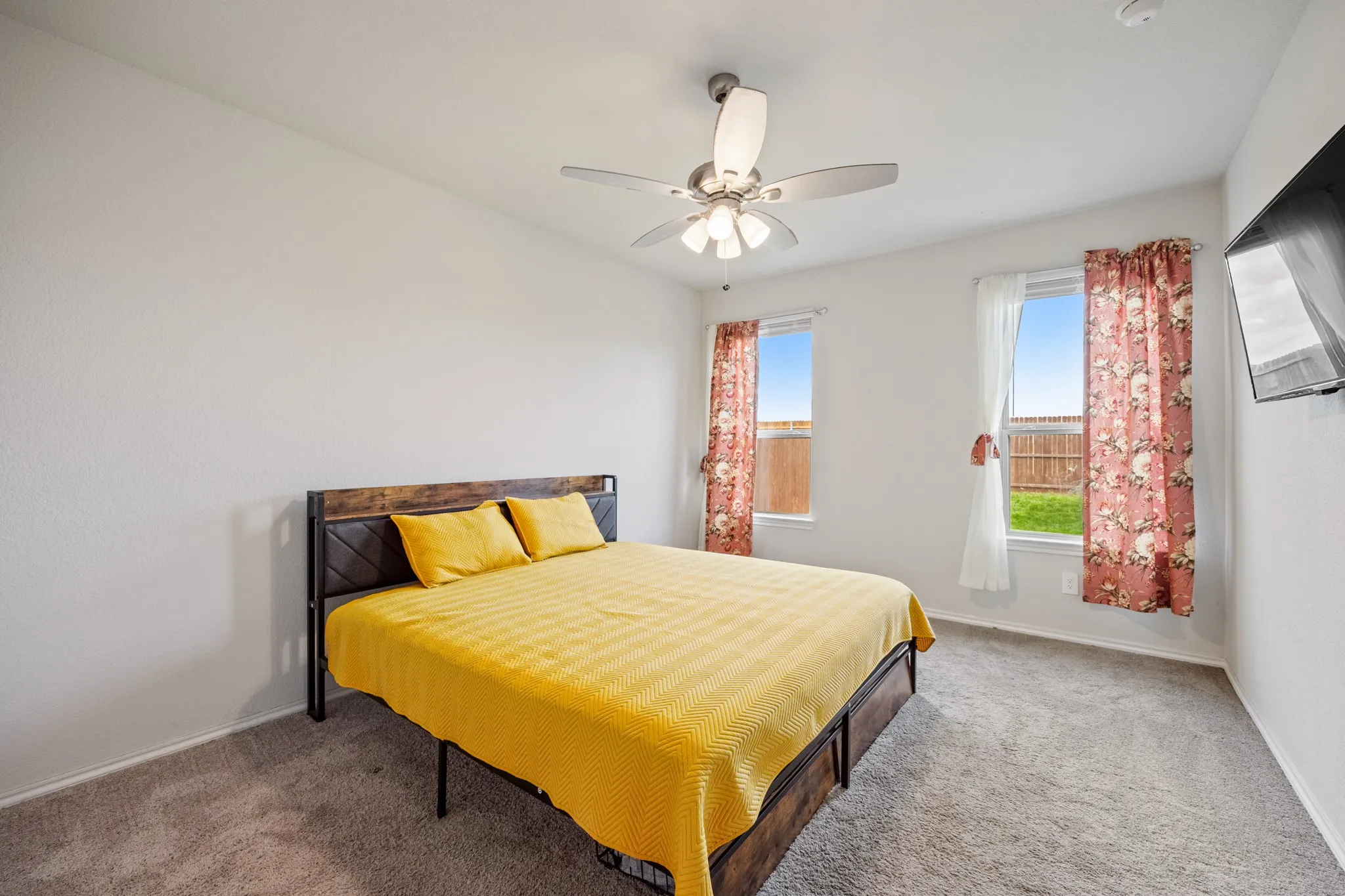 Soft gray carpeting, white walls, two windows, and a ceiling fan with integrated lighting