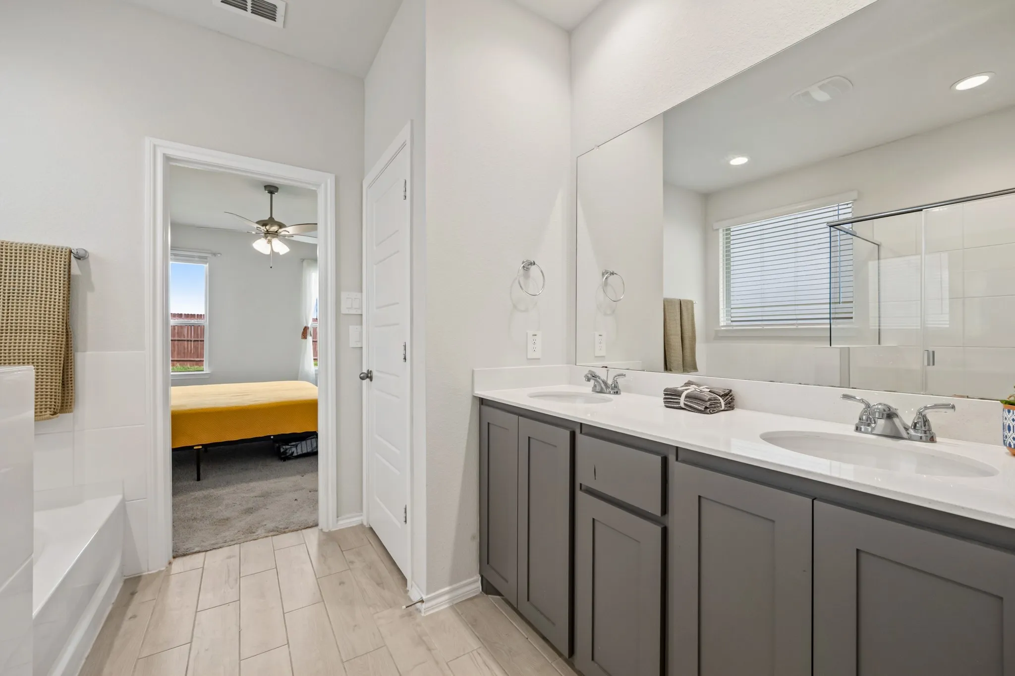 Double vanity with a white countertop and undermount sinks, wood-finish flooring, and a built-in bathtub with white tile surround