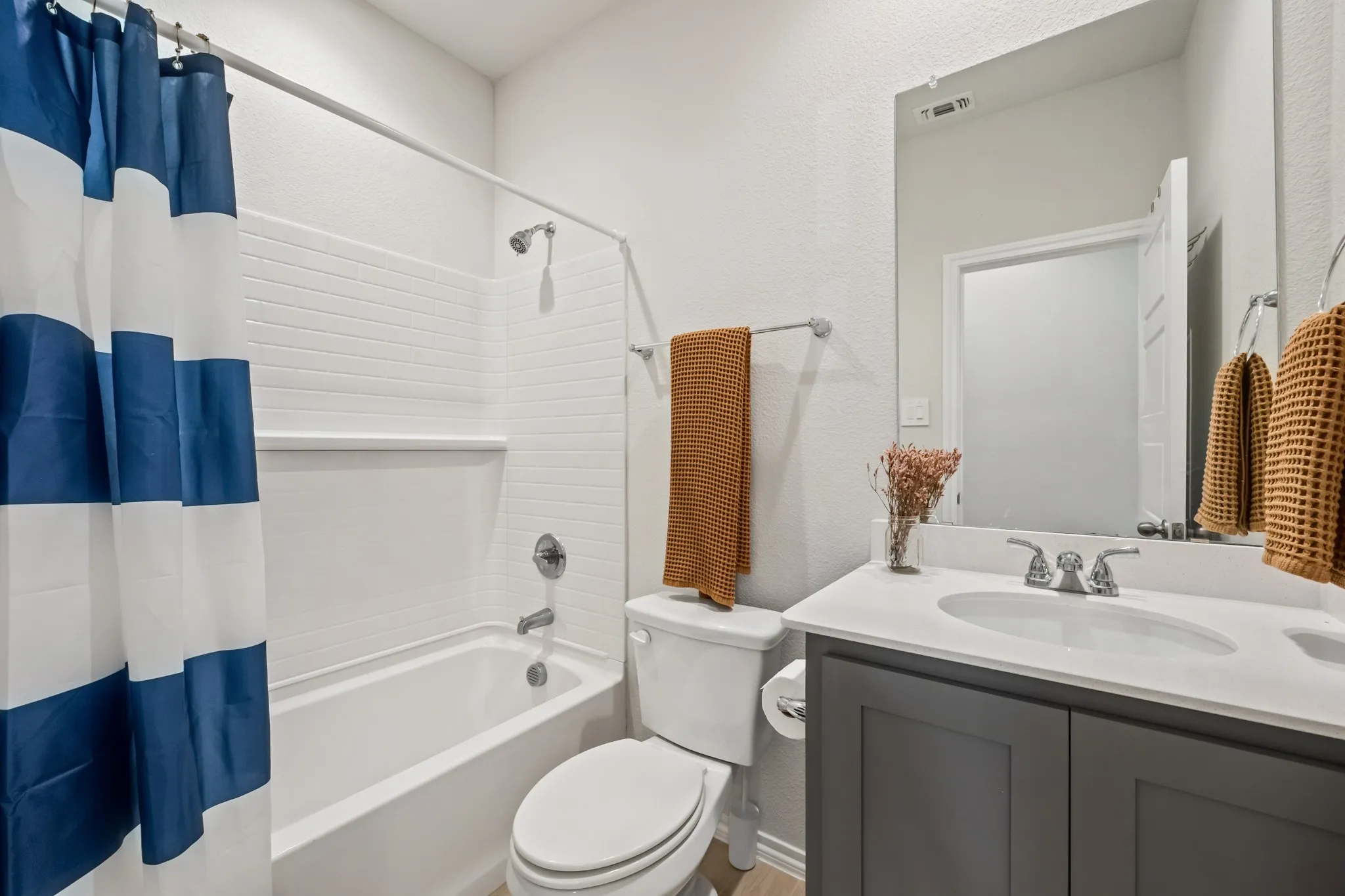White subway tile shower surround, chrome shower fixtures, white bathtub, gray vanity with white countertop, and chrome vanity faucet