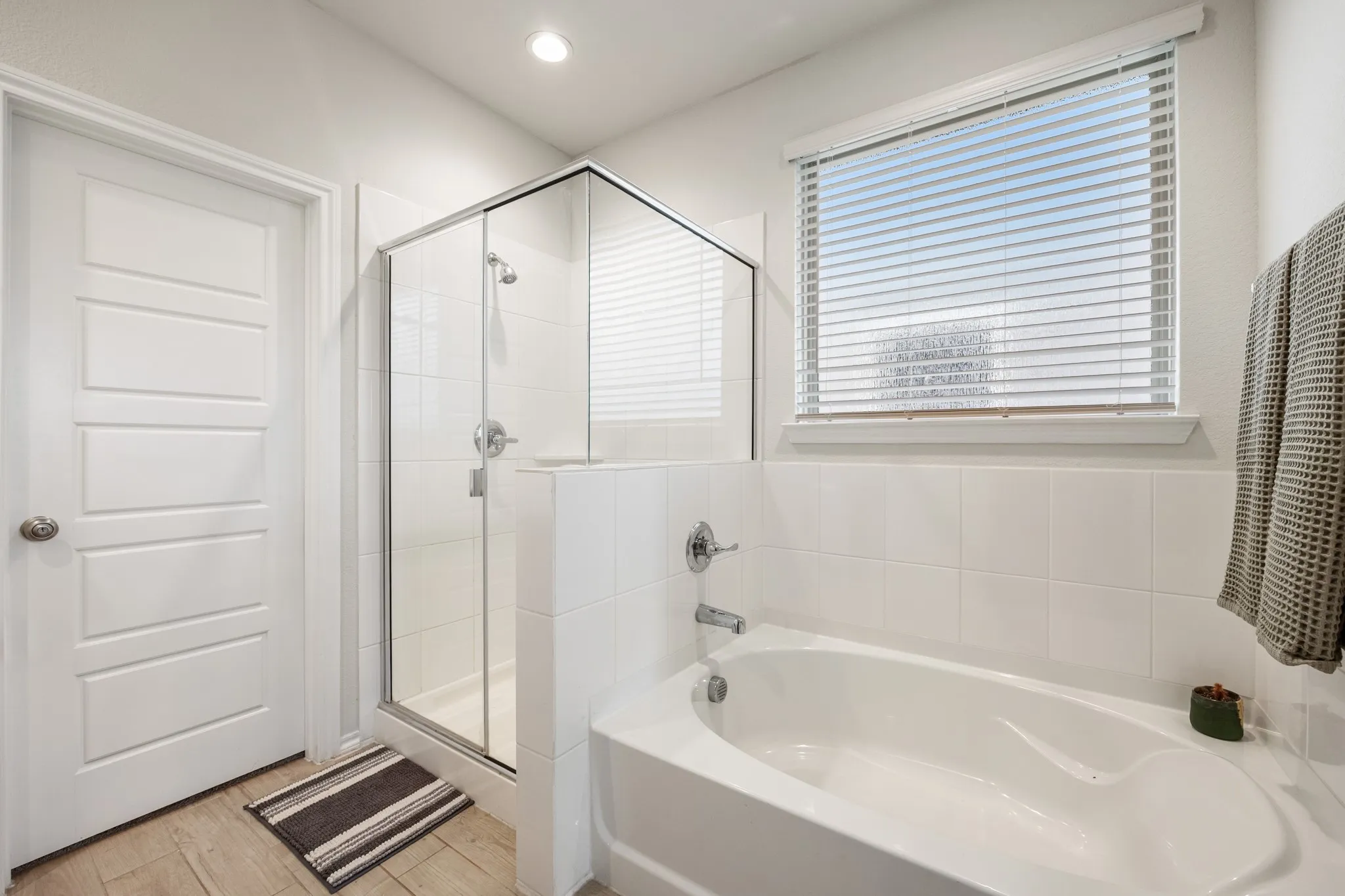 Recessed lighting, wood-finish flooring, glass-enclosed shower, built-in bathtub, and horizontal window blinds