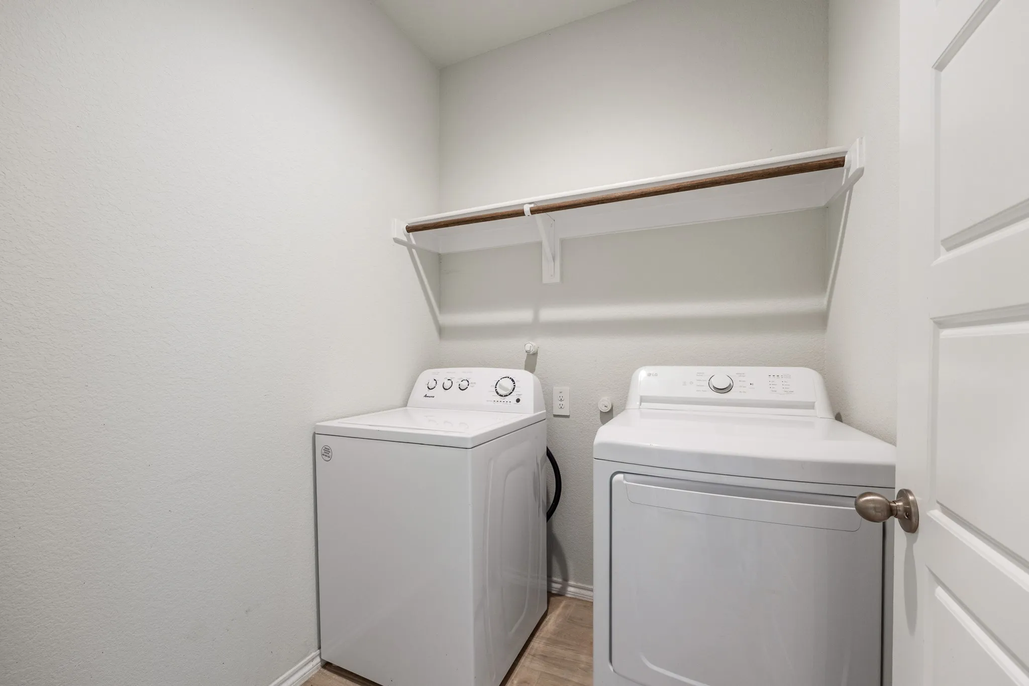 Dedicated laundry area featuring a wall-mounted shelf with a hanging rod and wood-finish flooring