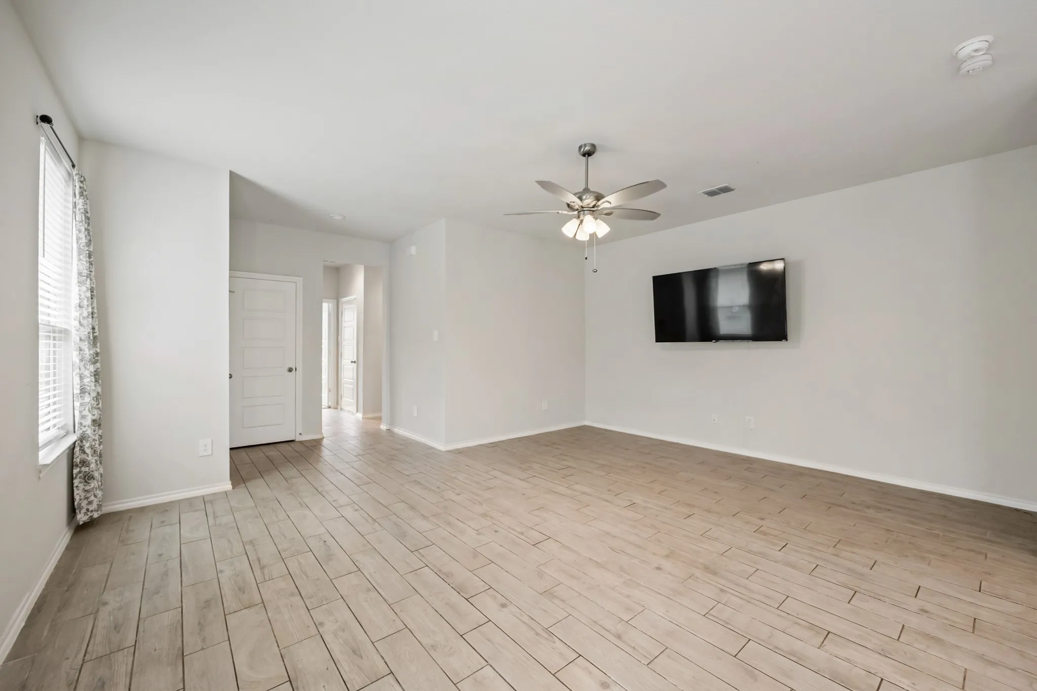 Spacious room featuring wood-finish flooring, ceiling fan with integrated lighting, and neutral wall paint