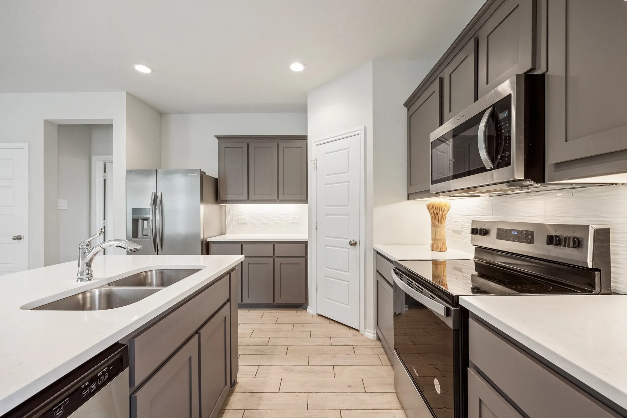 Kitchen featuring stainless steel appliances, grey cabinetry, white countertops, tile backsplash, and wood-finish flooring