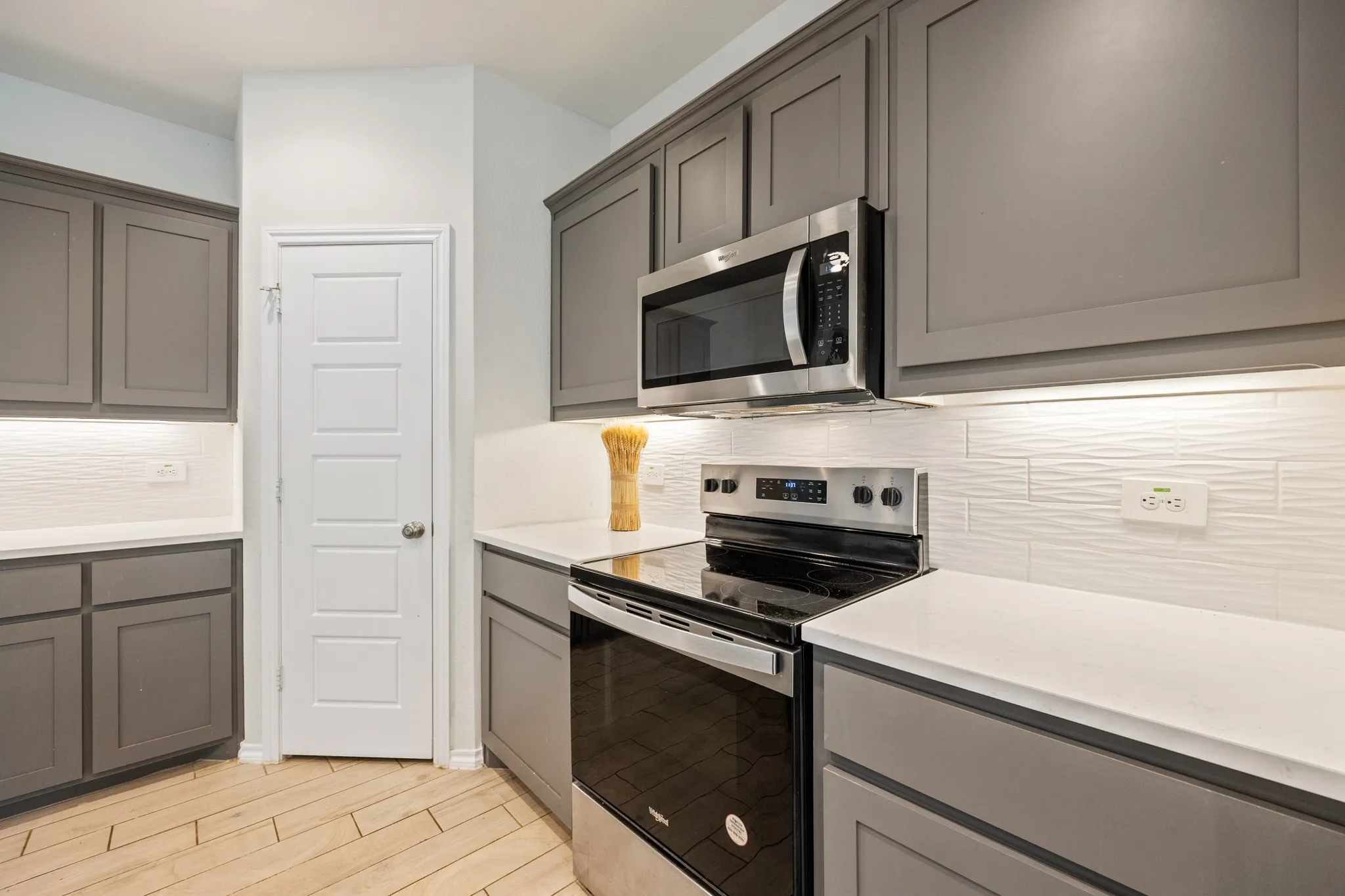 Contemporary kitchen featuring gray cabinetry, white countertops, textured white tile backsplash, stainless steel appliances, and wood-finish flooring
