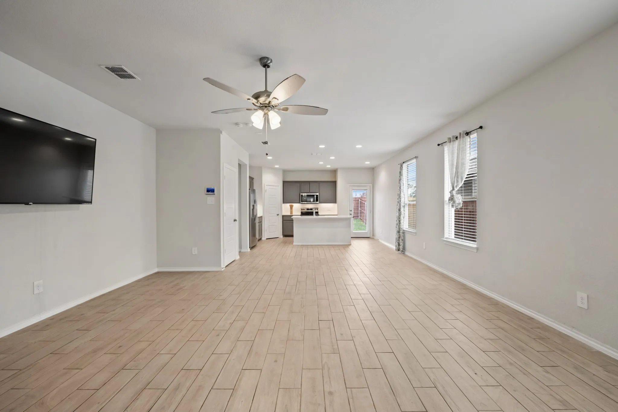 Expansive living area with wood-finish flooring, recessed lighting, and a ceiling fan