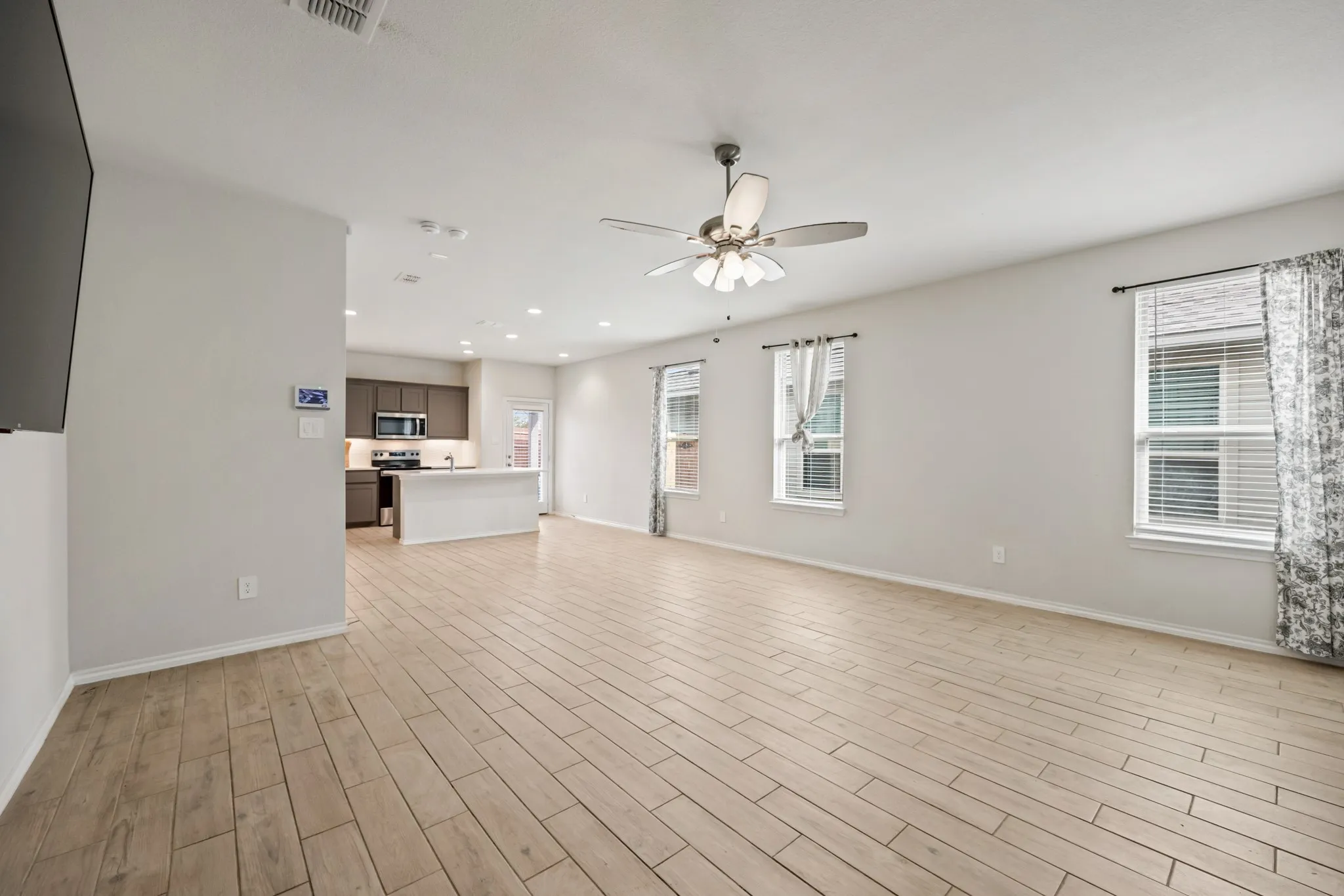 Spacious open-concept living area featuring wood-finish flooring, recessed lighting, and a ceiling fan