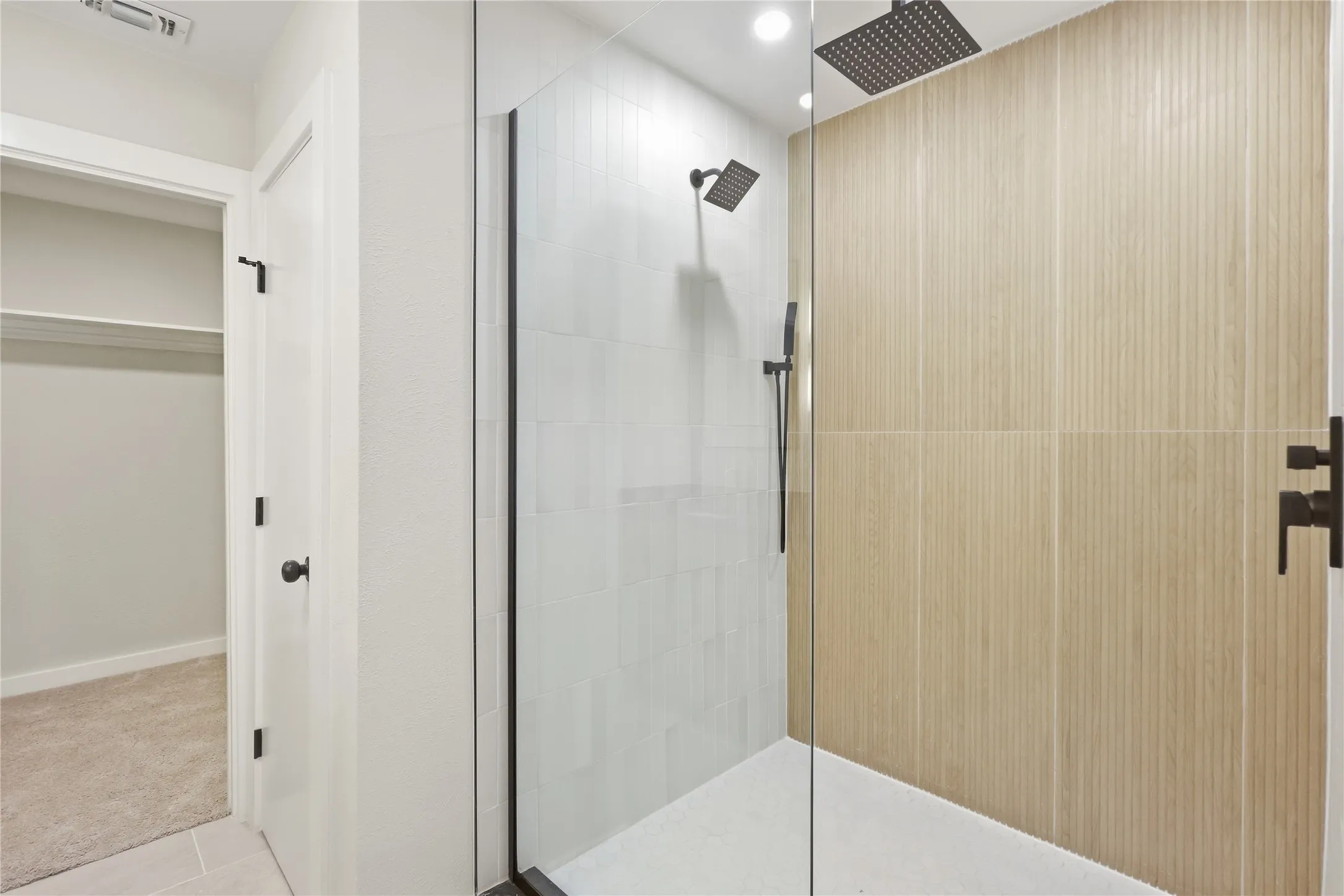 Glass-enclosed shower with matte black fixtures, rain shower head, and vertical plank-style wall tiling