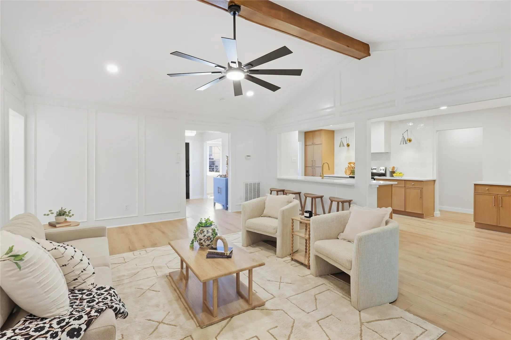 Vaulted ceiling with exposed wood beam, recessed lighting, wood-finish flooring, white paneling, and an open concept kitchen with light wood cabinetry