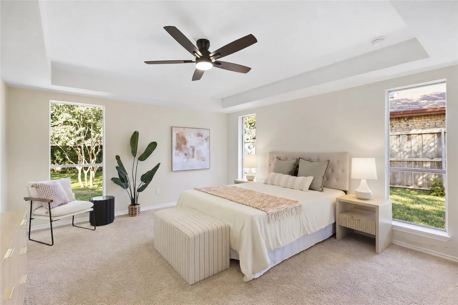 Recessed tray ceiling with crown molding, carpeted flooring, multiple rectangular windows, and a ceiling fan with integrated lighting