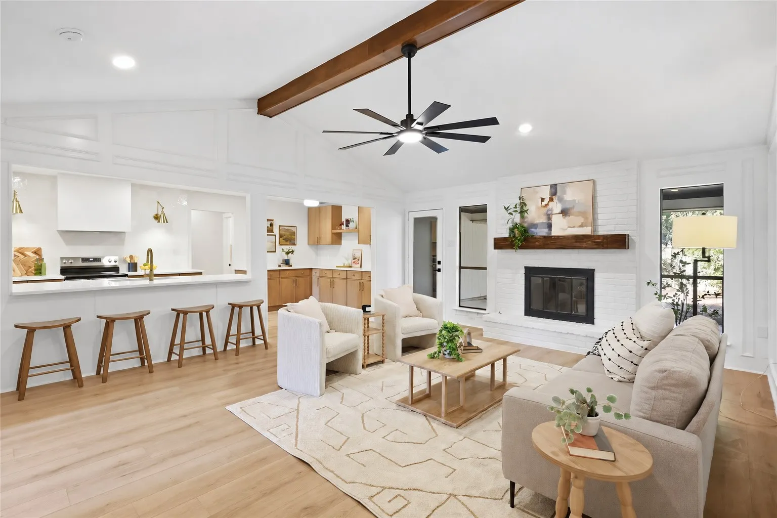 Vaulted ceilings with exposed wood beams, wood-finish flooring, a white brick fireplace with a wood mantel, a kitchen island with seating, and wood cabinetry