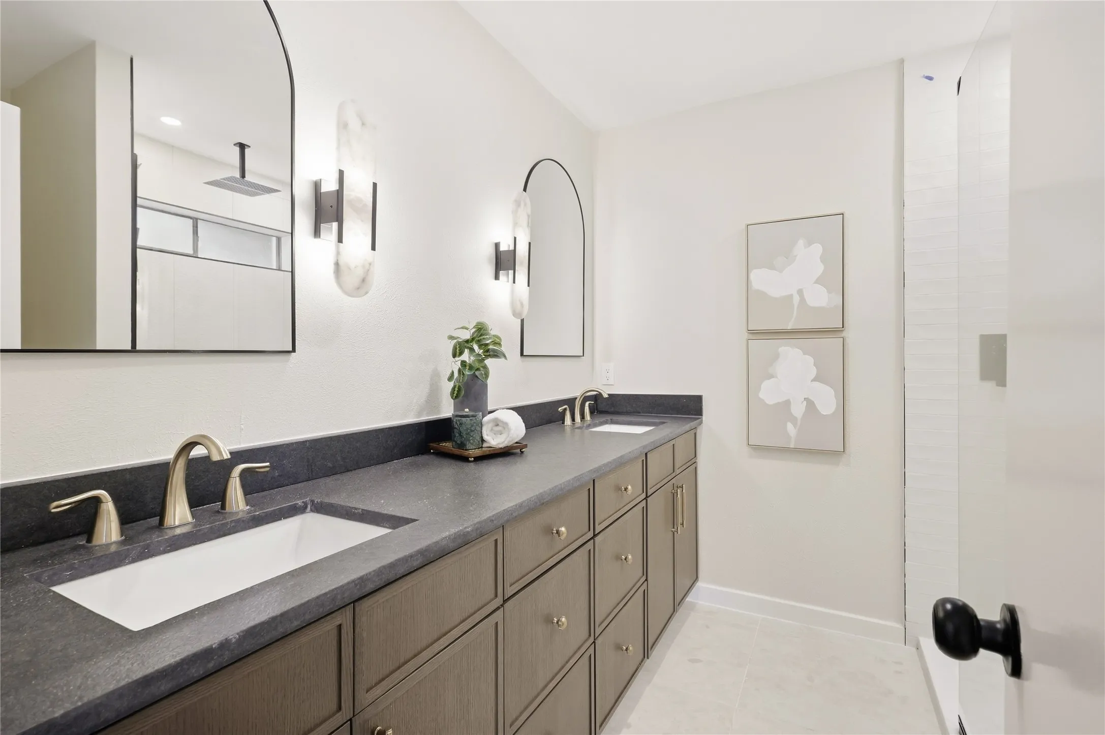 Dual recessed sinks with gold-toned fixtures, dark-toned vanity with multiple drawers, dark countertop, and decorative wall sconces