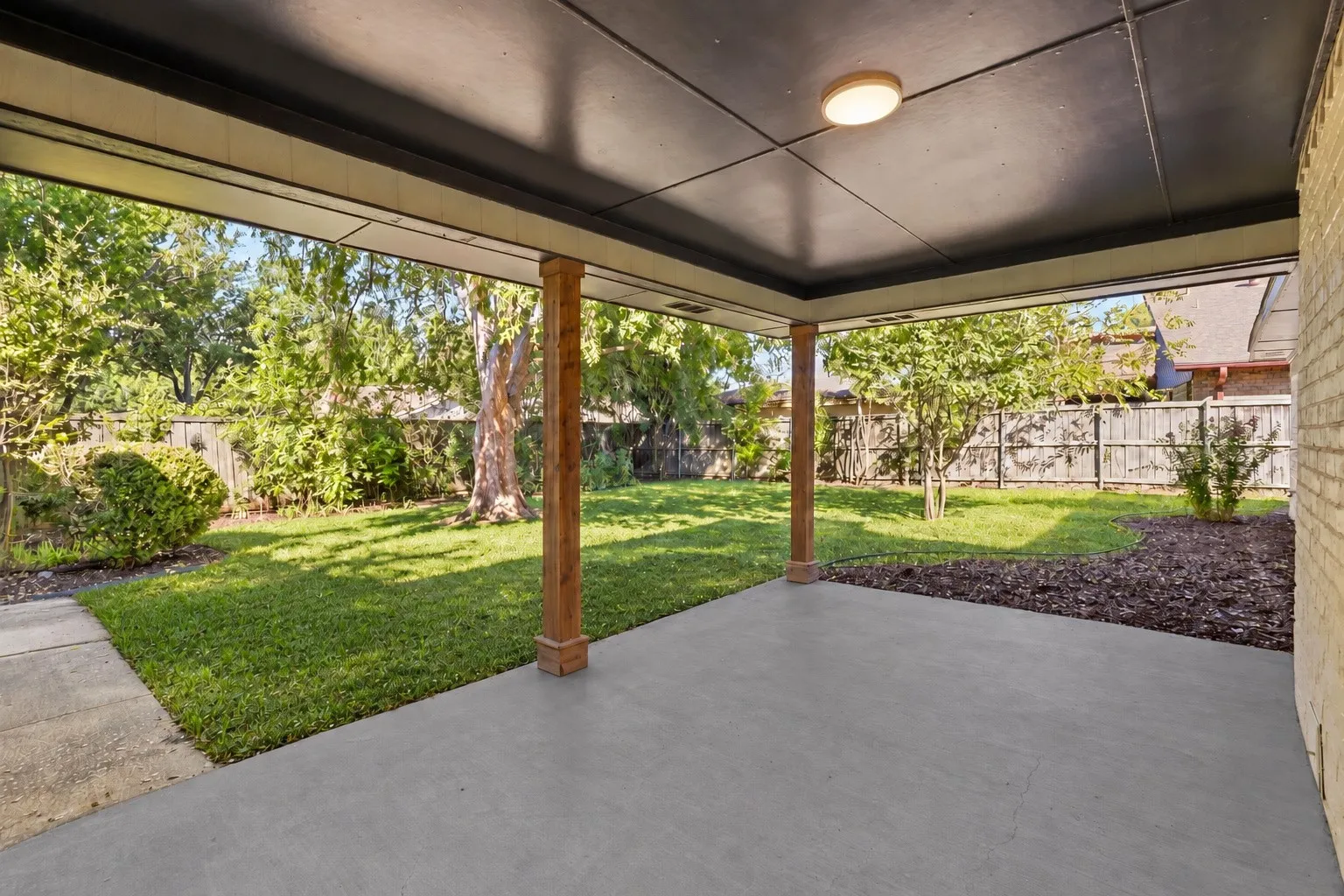 Covered patio with a concrete surface, wood-finish support columns, a ceiling-mounted light fixture, and a brick exterior wall