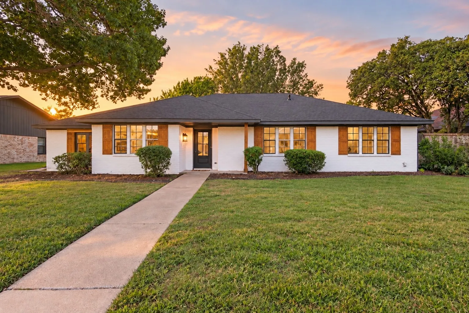 White brick exterior with dark shingle roofing, wood-look window shutters, and a black front entry door