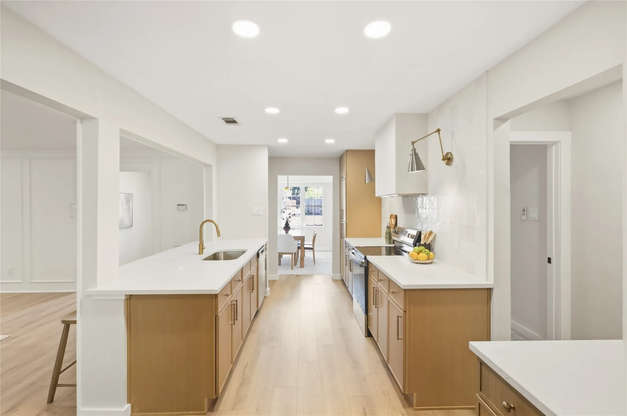Galley kitchen featuring light wood-finish cabinetry, white countertops, stainless steel appliances, and a tile backsplash