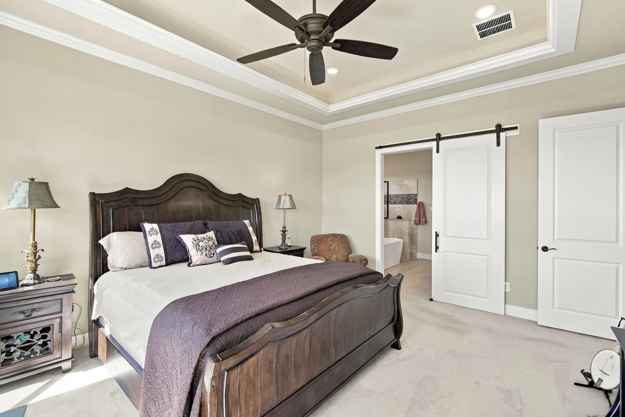 Another view of the trey ceiling with the cove lighting, crown molding, ceiling fan, recessed lighting and a barn door leading to the ensuite bath.