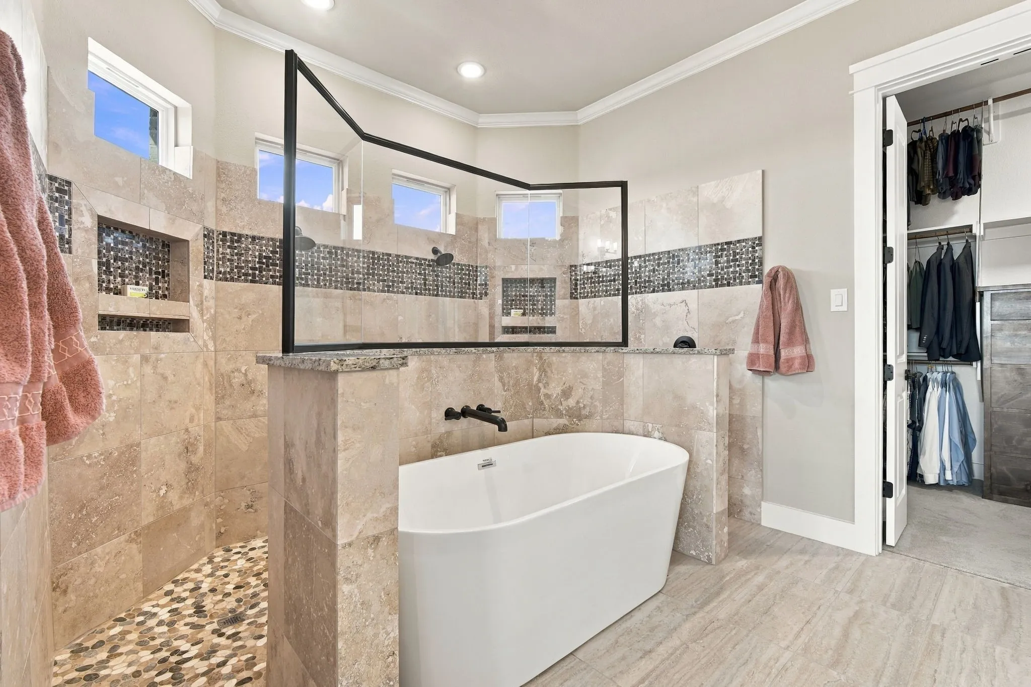 Freestanding tub with matte black fixtures, tiled walk-in shower with built-in niches, dual shower heads and a full walk-in closet with built-in shelving and drawers.