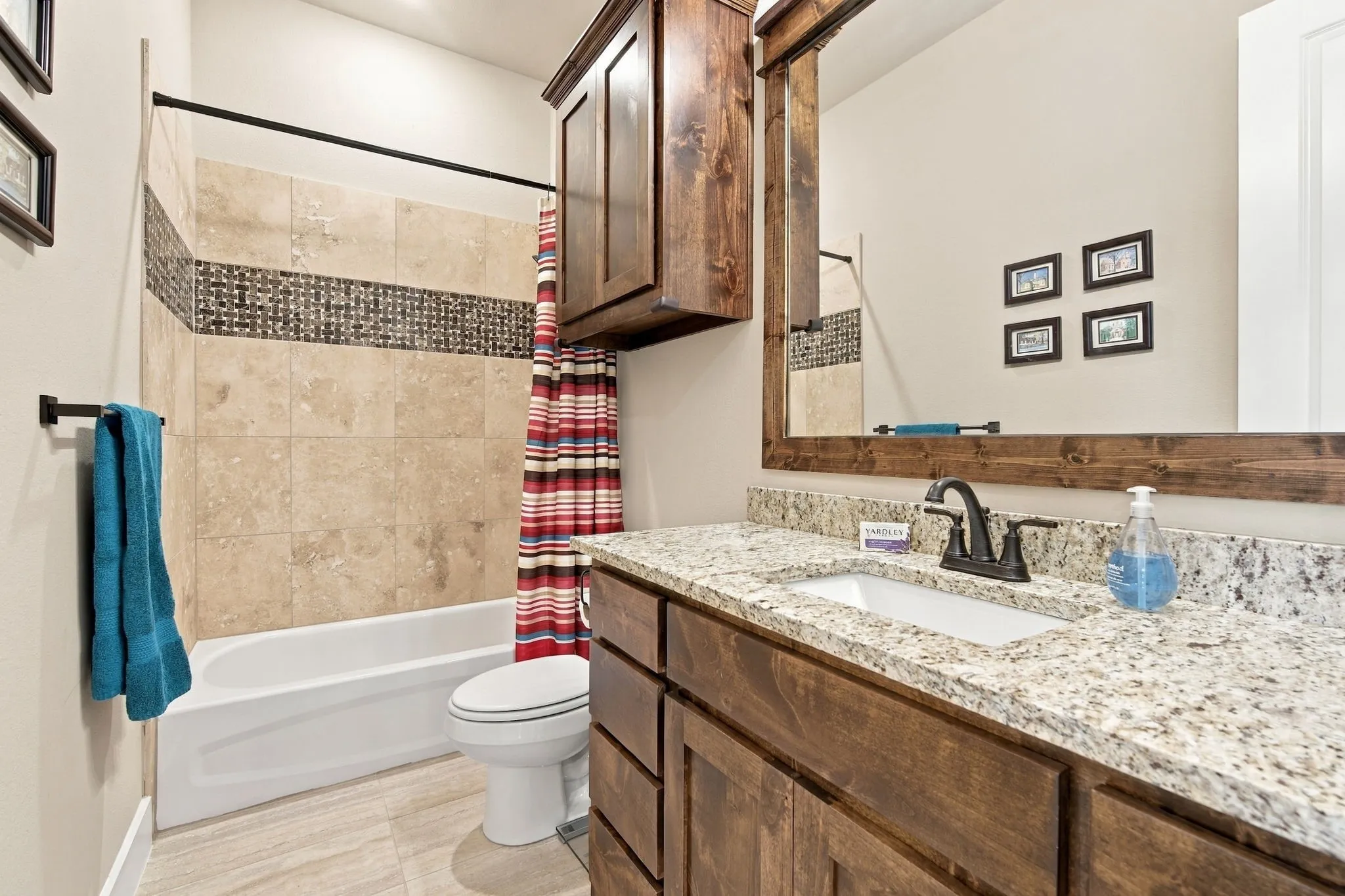 Built-in vanity with a granite countertop, rectangular undermount sink, decorative tile in the bathtub and a framed mirror adorn this bathroom.