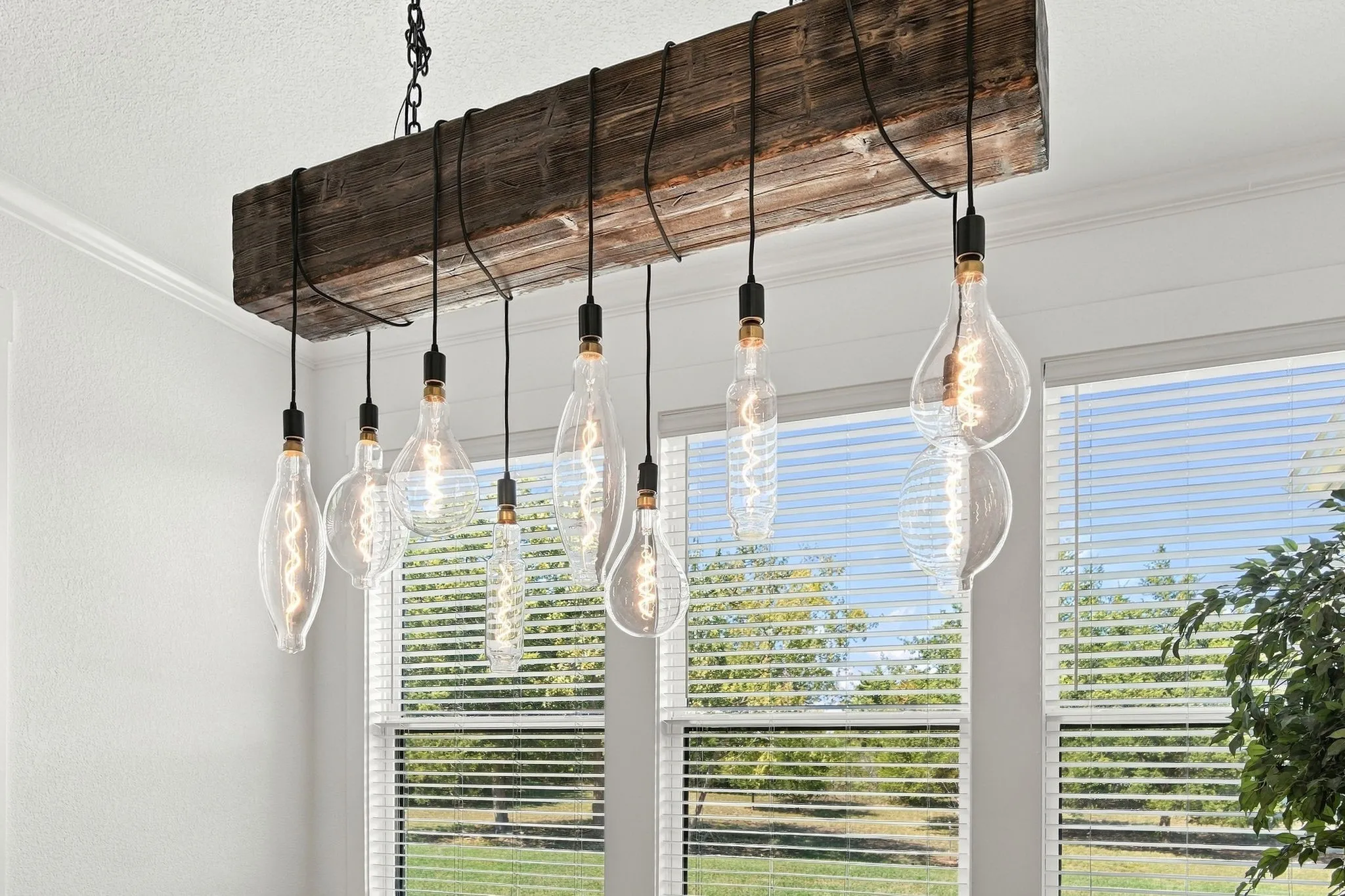 Exposed wood beam chandelier with multiple Edison-style bulbs, crown molding, and large windows to let in natural light.