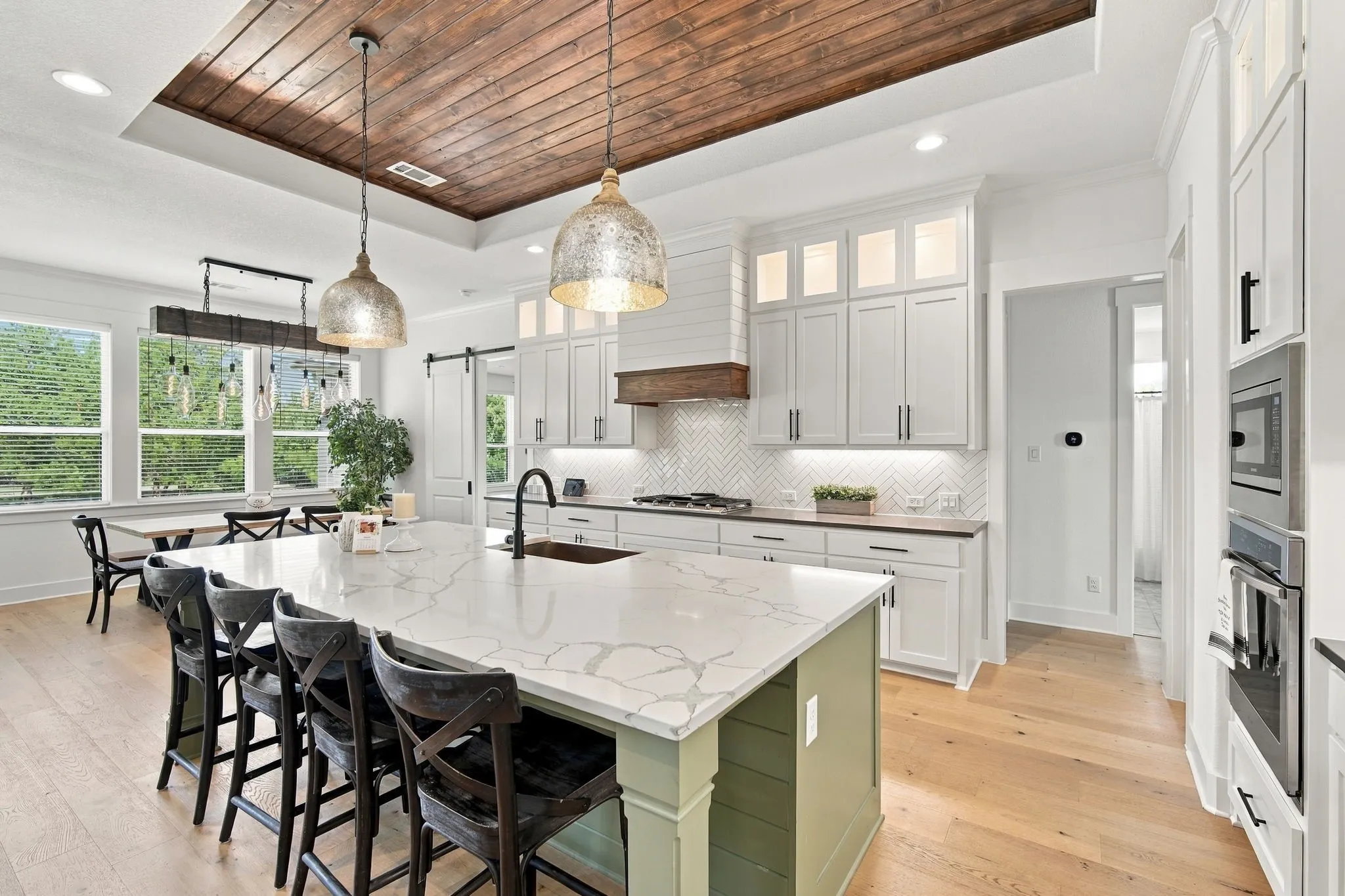 Gourmet kitchen has a 5 burner gas cooktop, herringbone tile backsplash, large central island with seating and a copper farmhouse sink.