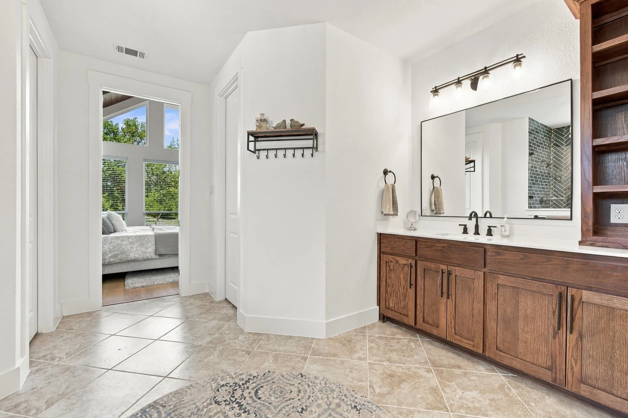 Tile flooring with a diamond pattern, wood-finish vanity with a white countertop, built-in open shelving, and a large rectangular mirror with wall-mounted lighting