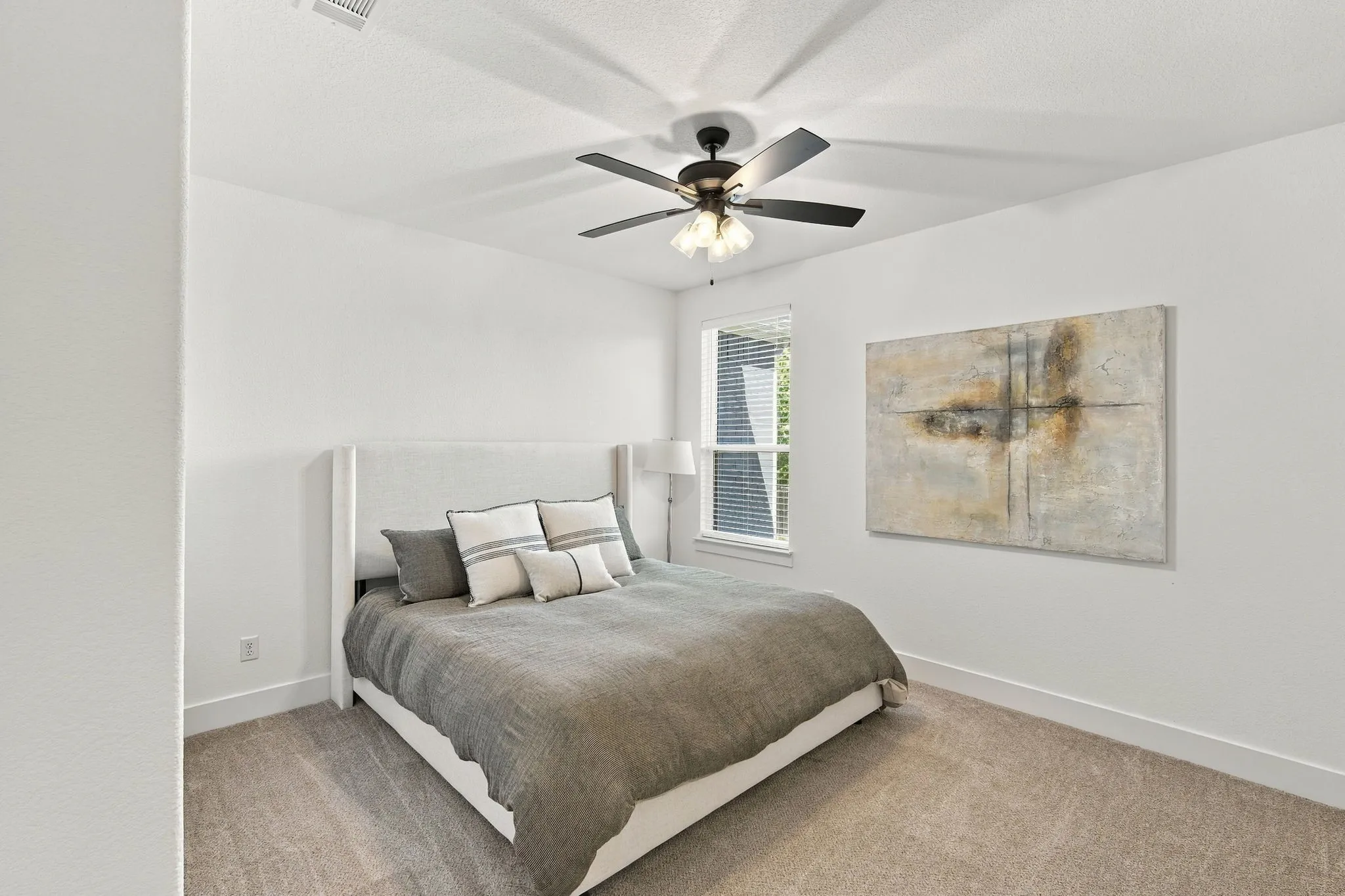 Spacious bedroom with a walk in closet, blinds and a ceiling fan.