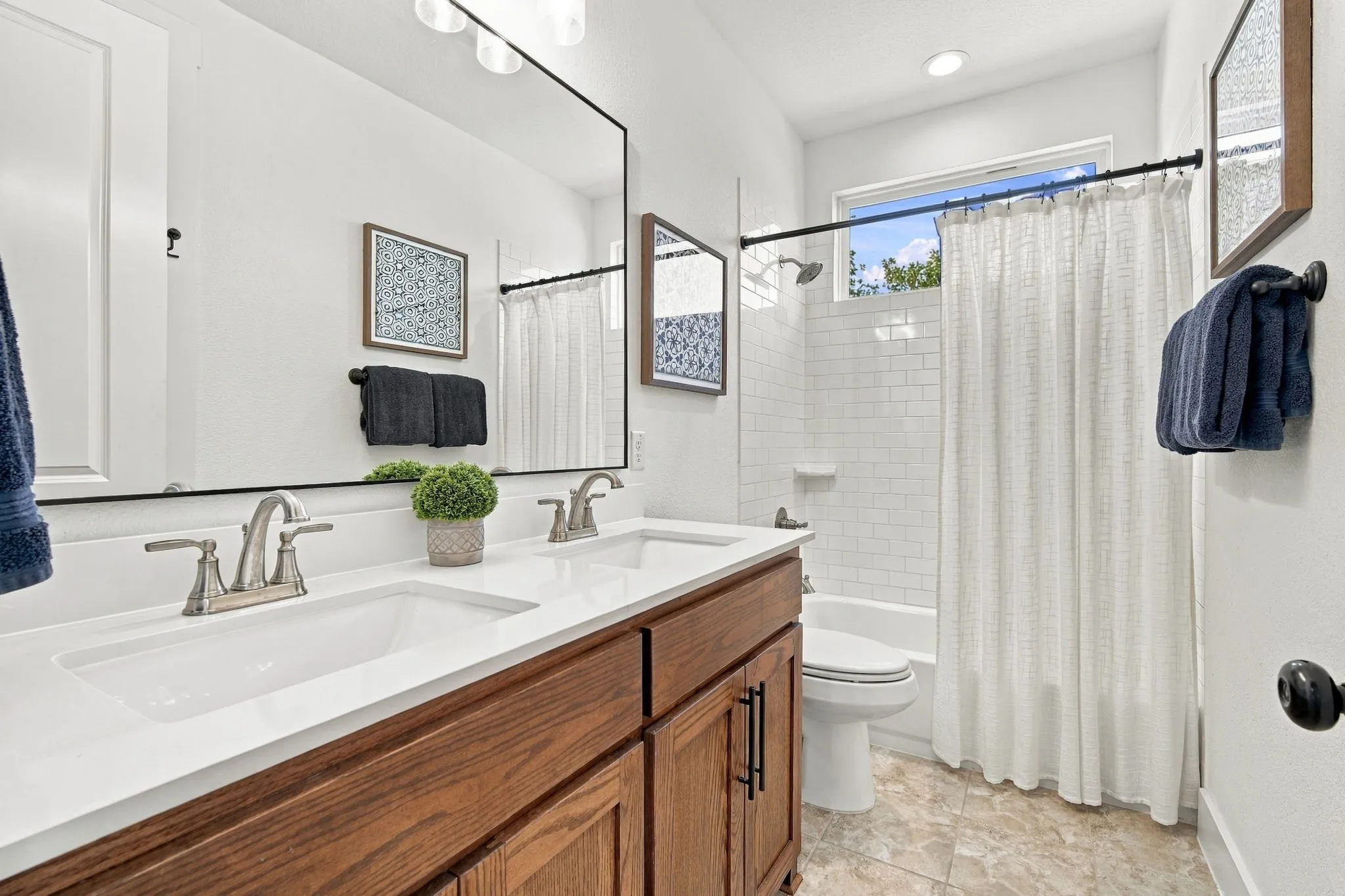 Nice secondary bath with a dual vanity with undermount sinks, shaker style wood cabinetry, a large frameless mirror, a shower-tub combination with subway tile surround, and tiled flooring